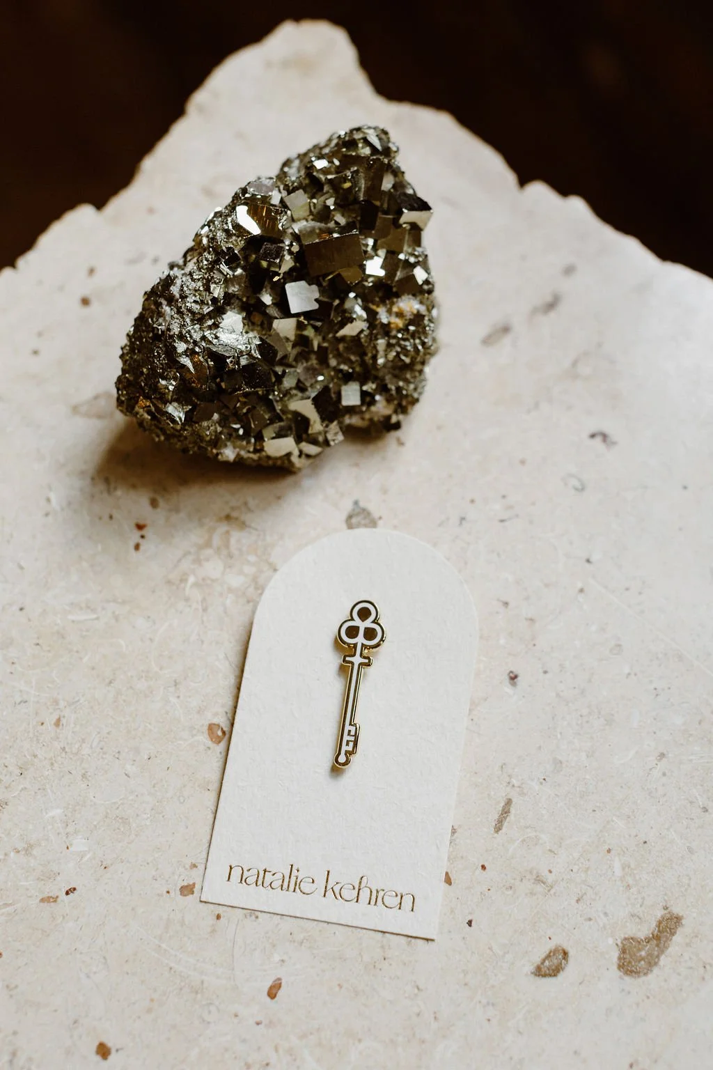 Natalie Kehren branded key pin on a logo card beside a pyrite crystal, brand collateral designed by Moonstone Creative