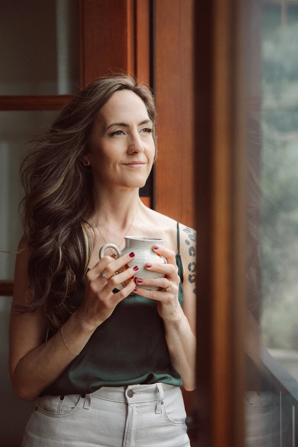 Miranda Braithwaite, founder of Moonstone Creative, holding a ceramic mug and gazing out a window