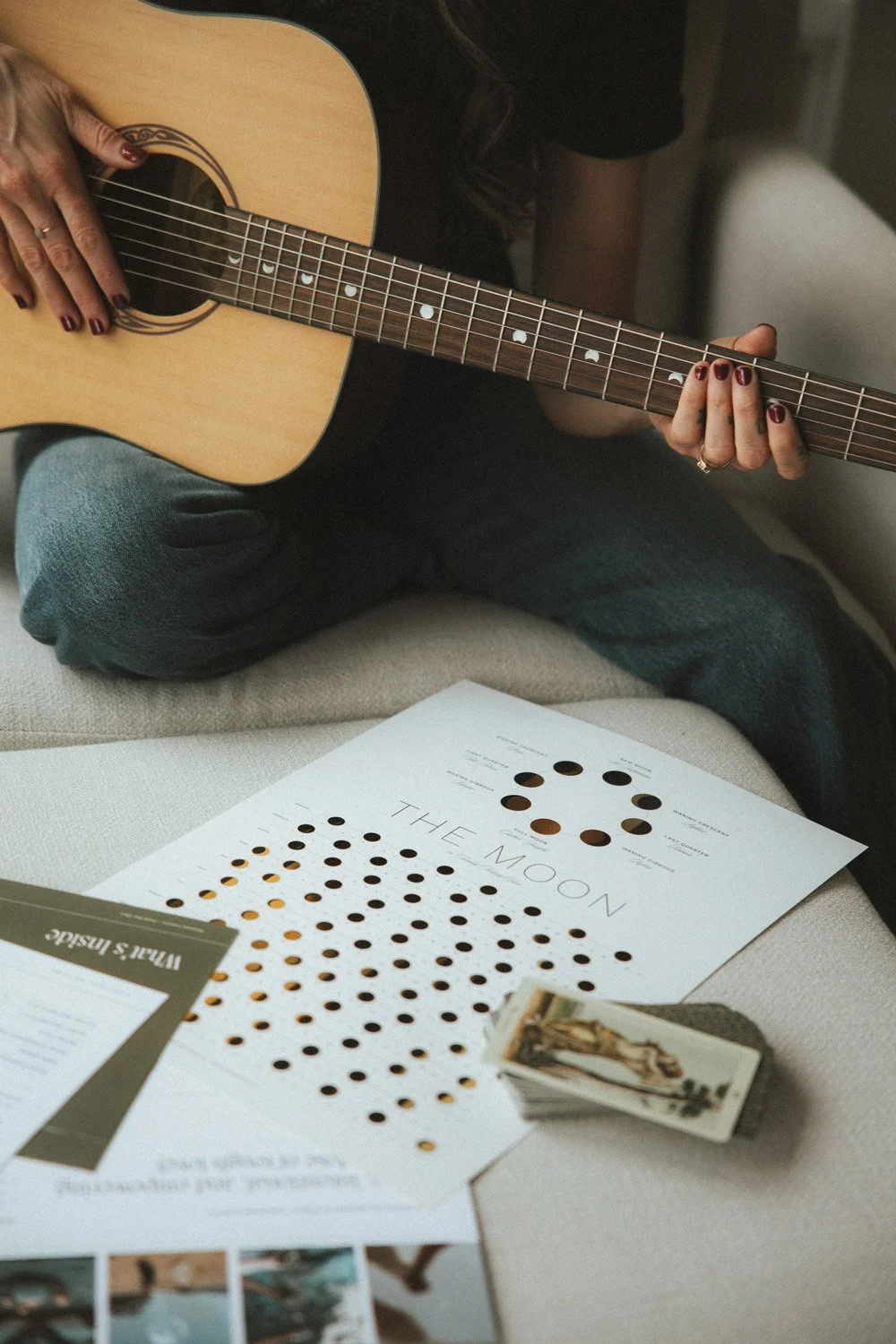 Moonstone Creative Brand Star Chart documents, tarot cards, and a moon phase reference chart laid out on a sofa beside an acoustic guitar