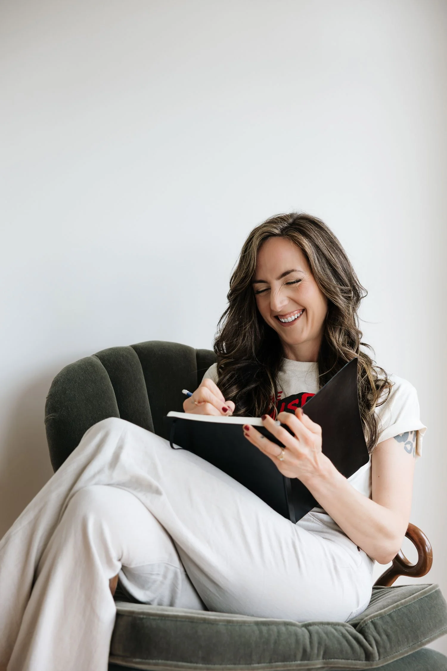 Miranda Braithwaite, Okanagan brand designer and founder of Moonstone Creative, laughing while writing in a notebook in a green velvet chair