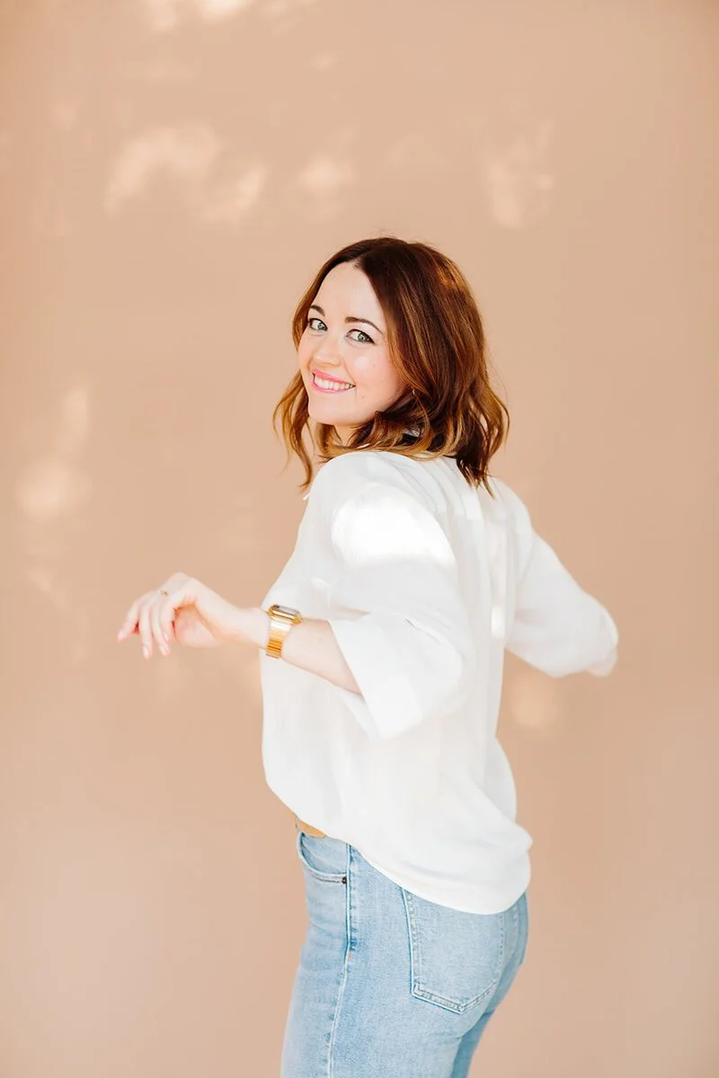 Jennifer Turner from Gemini Copy Co smiling over her shoulder in a white blouse against a warm beige studio background