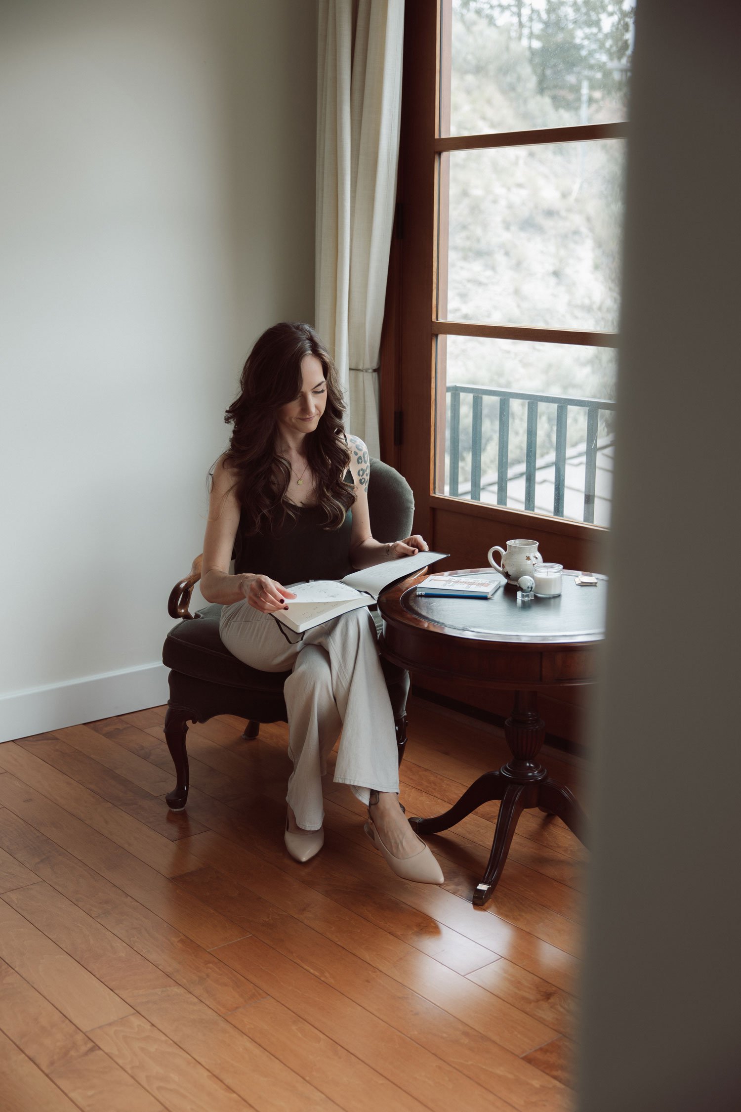 Miranda Braithwaite, Okanagan branding expert and founder of Moonstone Creative, reading in a green velvet chair beside a window and antique side table