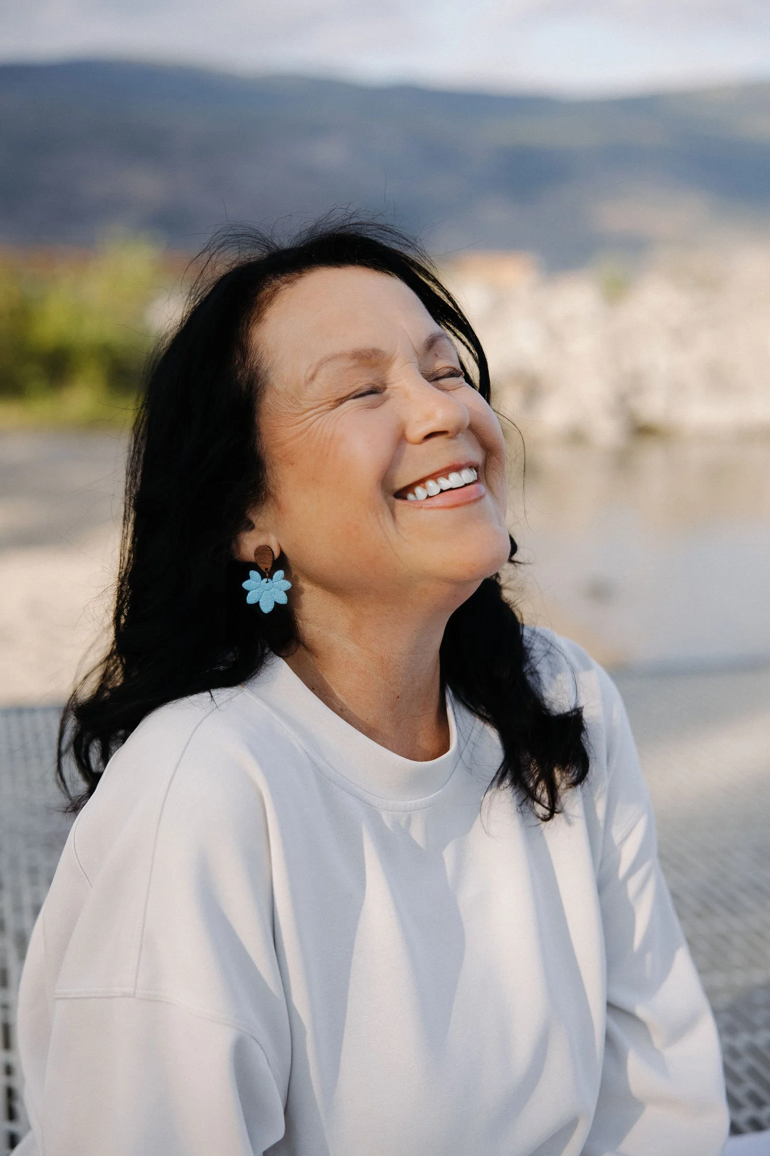 Janette Lippai, founder of Blue Heron Block Therapy, laughing outdoors with a lake and mountains in the background