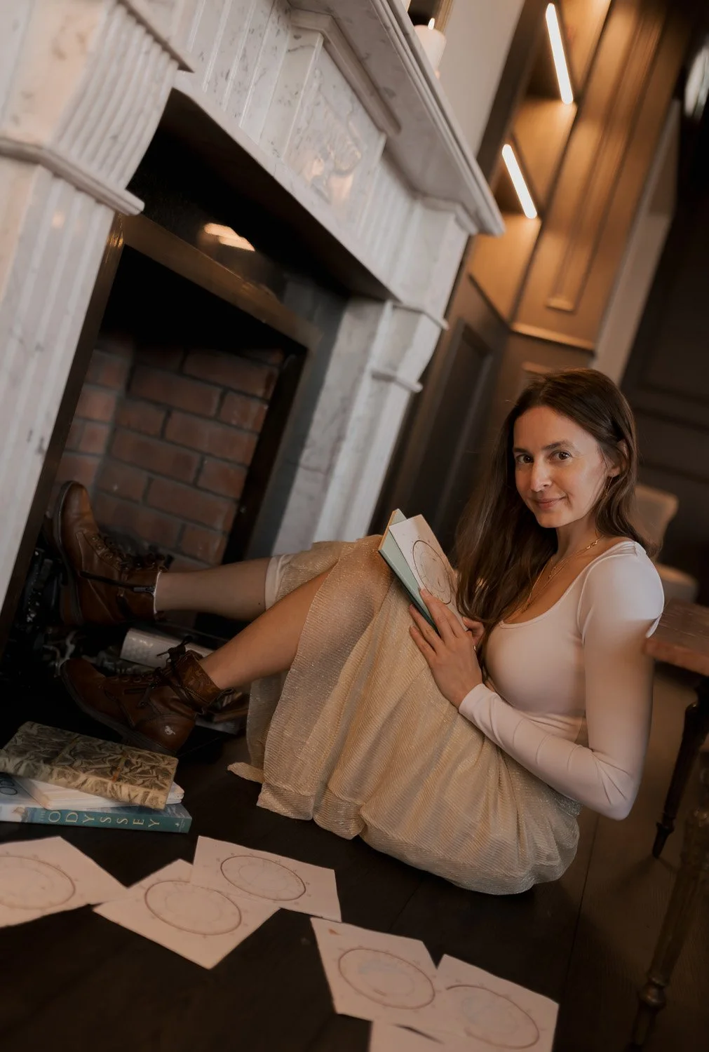 Rachelle Hicks of Rachelle Hicks Astrology seated by a marble fireplace surrounded by brand logo sketches, photographed during her Moonstone Creative brand shoot