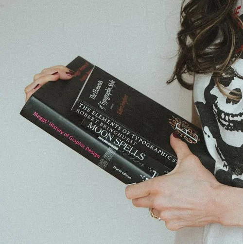 Miranda Braithwaite, Okanagan brand designer and founder of Moonstone Creative, holding typographic design books including Moon Spells and Elements of Typographic Style
