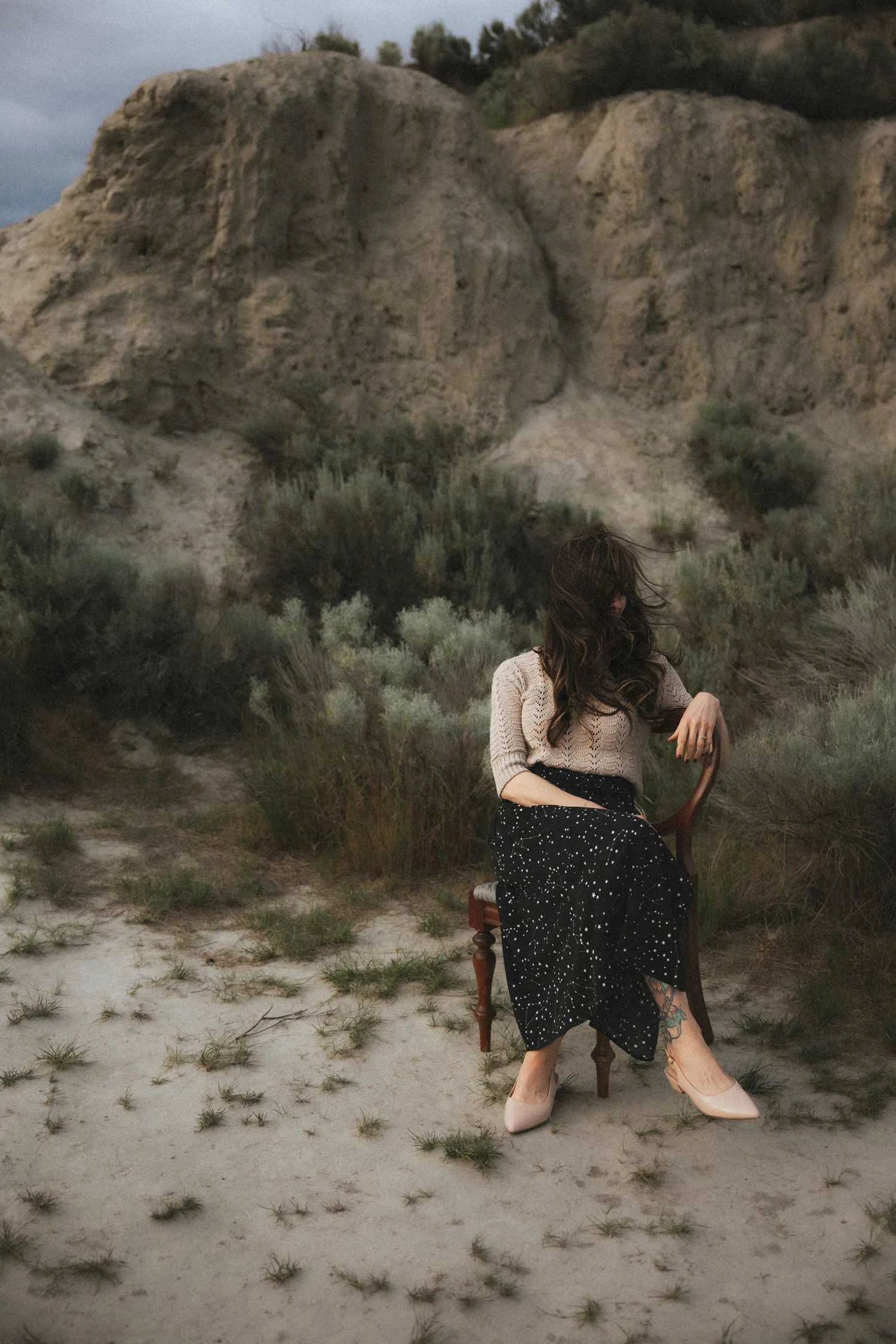 Miranda Braithwaite, founder of Moonstone Creative, seated in a wooden chair in the Okanagan Valley desert landscape near Penticton BC in a constellation skirt