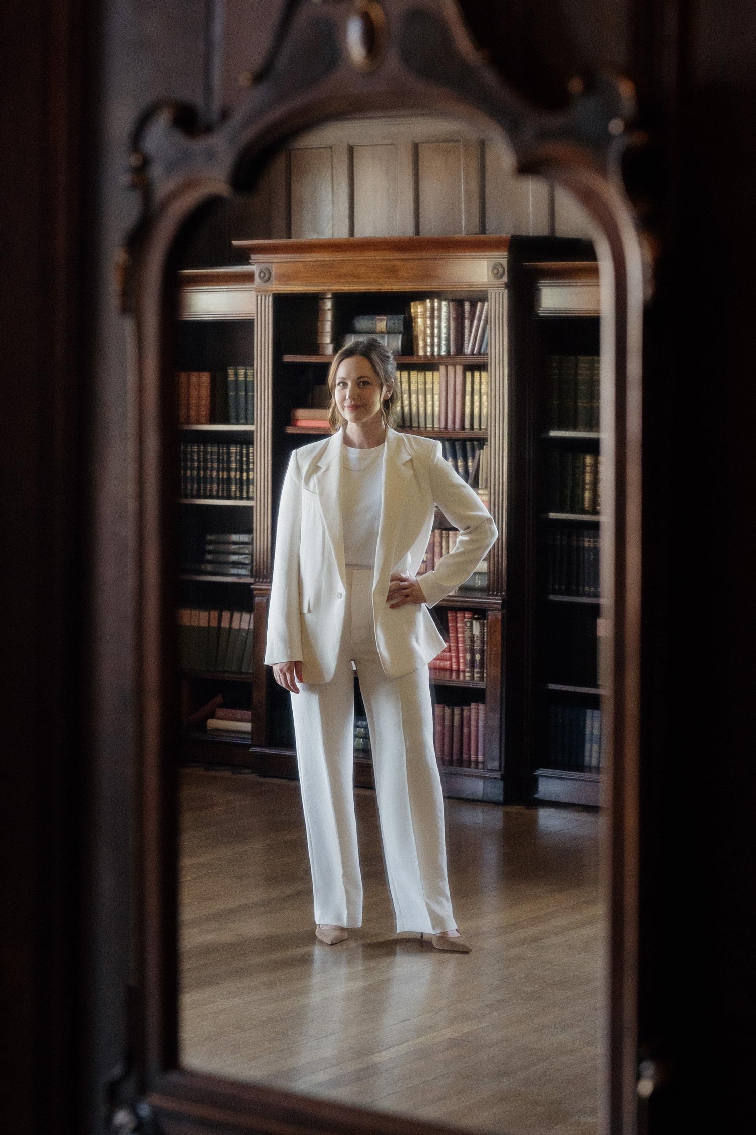 Jennifer Turner, founder of Gemini Copy Co, wears a cream power suit in a historic library full of books and an antique mirror