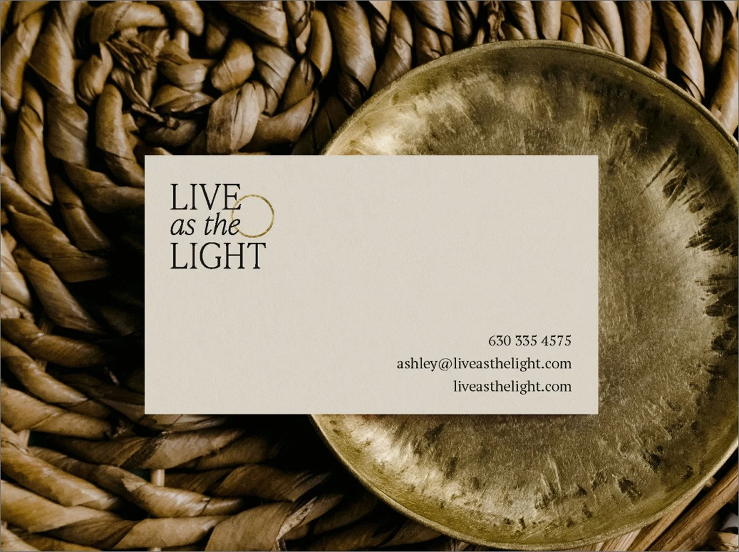 Live As The Light business card mockup in warm cream with gold circle logo detail on a woven textile and brass bowl background, designed by Moonstone Creative