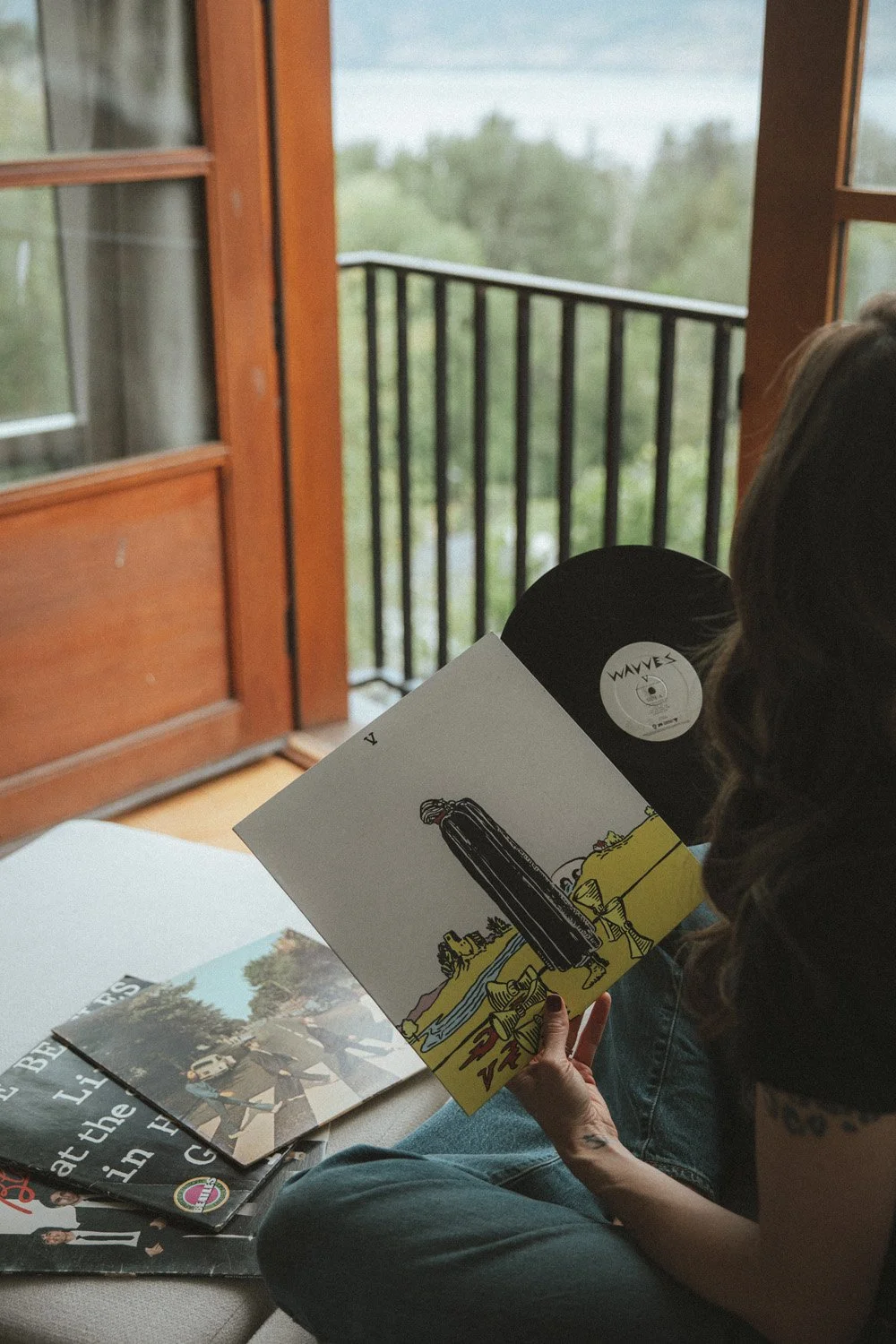 Miranda Braithwaite of Moonstone Creative browsing vinyl records including The Beatles Abbey Road by a lakeside window in the Okanagan