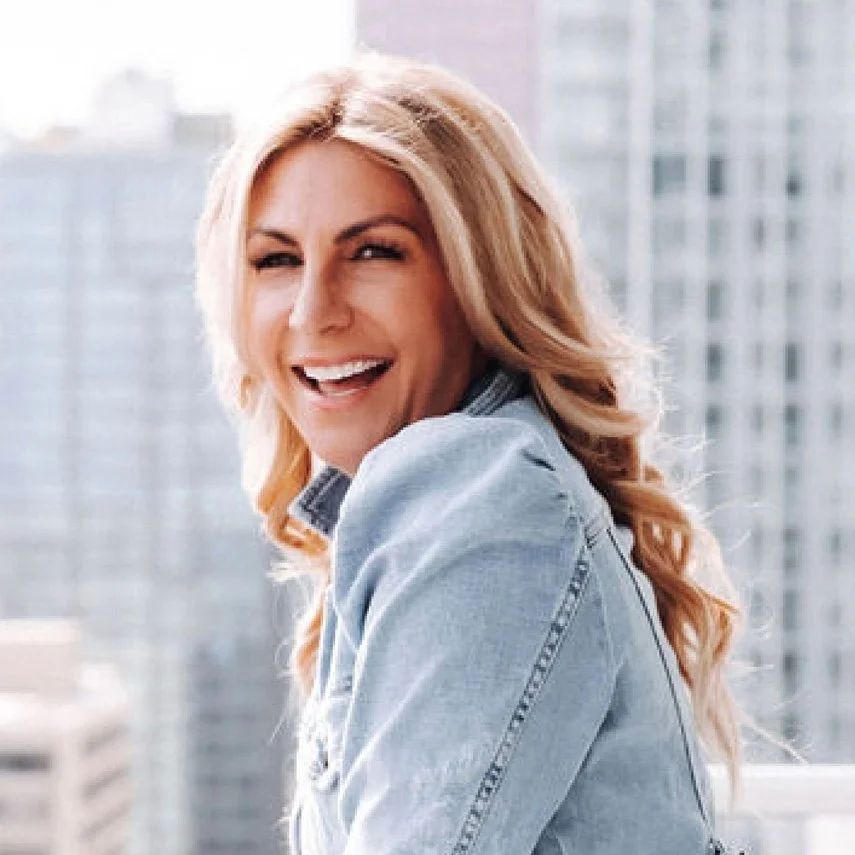 Jane Stoller founder of Organized Jane laughing on a rooftop balcony in a denim jacket with city skyline in the background