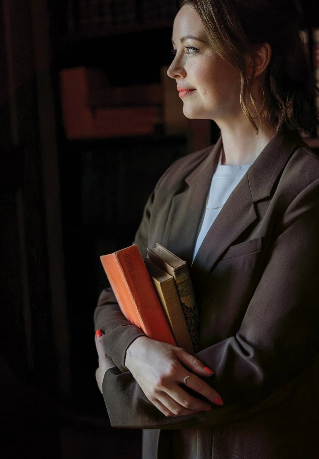 Jennifer Turner holding vintage books in a dark library for Gemini Copy Co’s brand photography