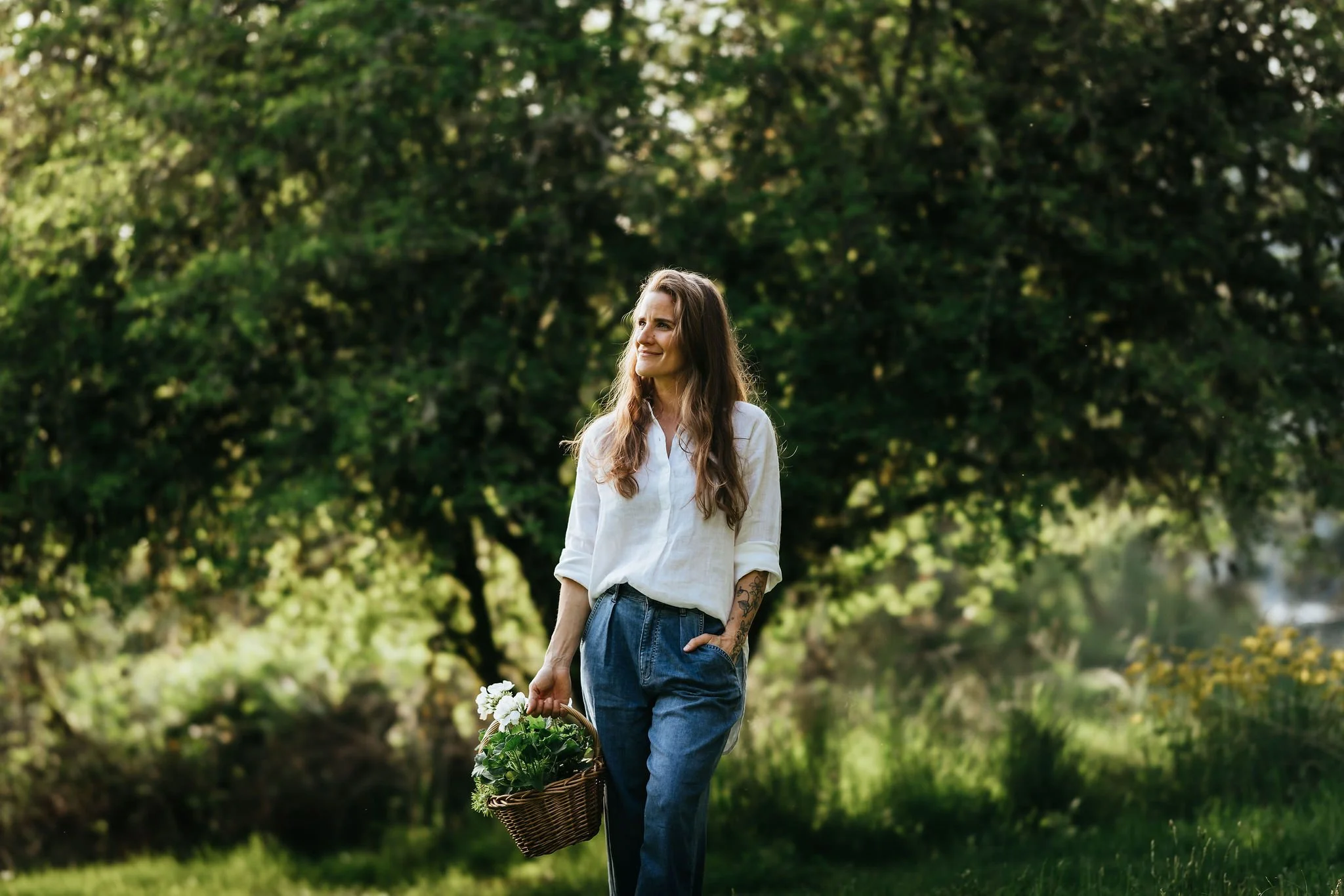 Alexandria Limberis, founder of Plants Become Art, walking through an orchard with a basket of flowers in hand