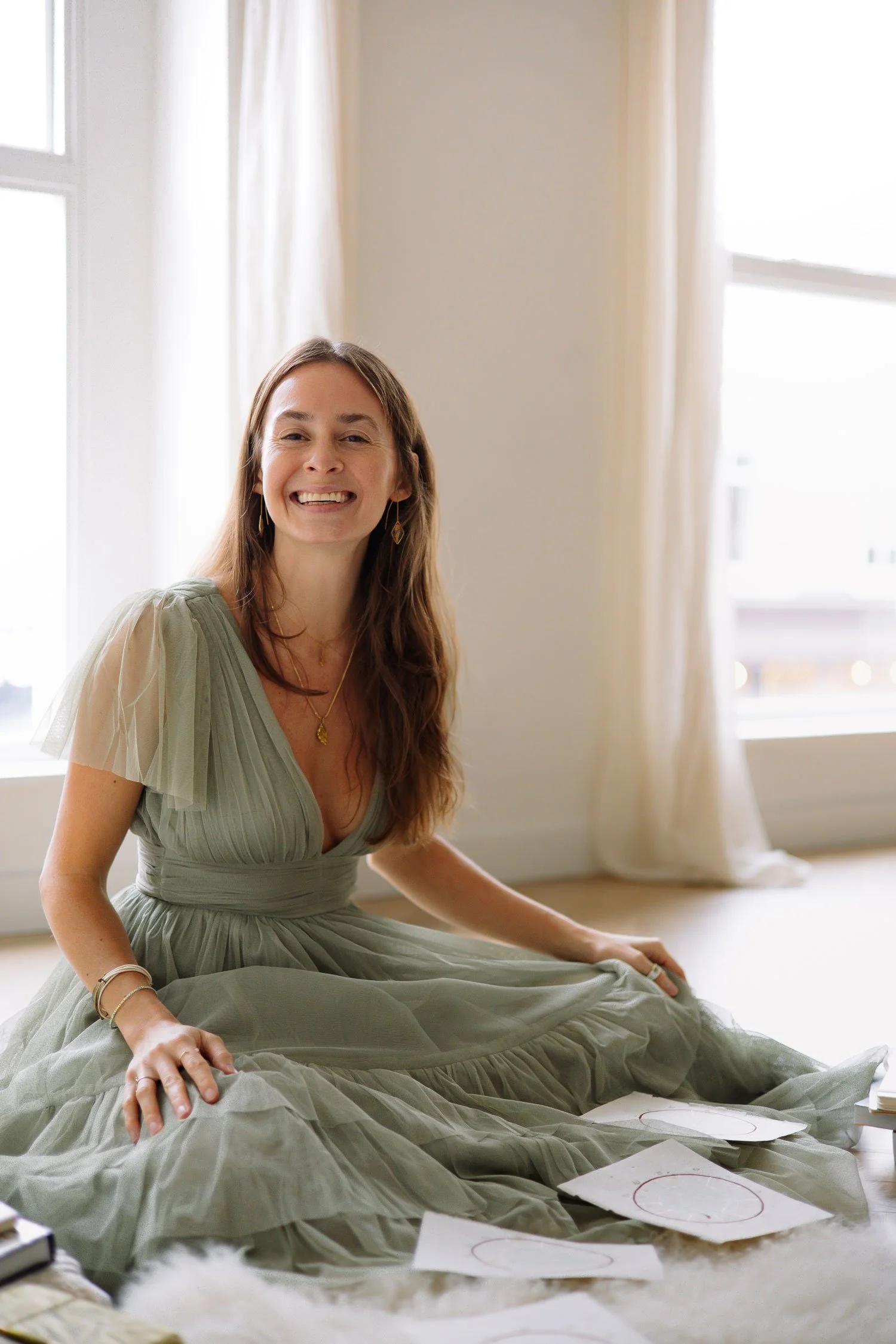 Rachelle Hicks of Rachelle Hicks Astrology laughing in a sage green tulle dress surrounded by natal chart sketches during her brand shoot, art directed by Moonstone Creative