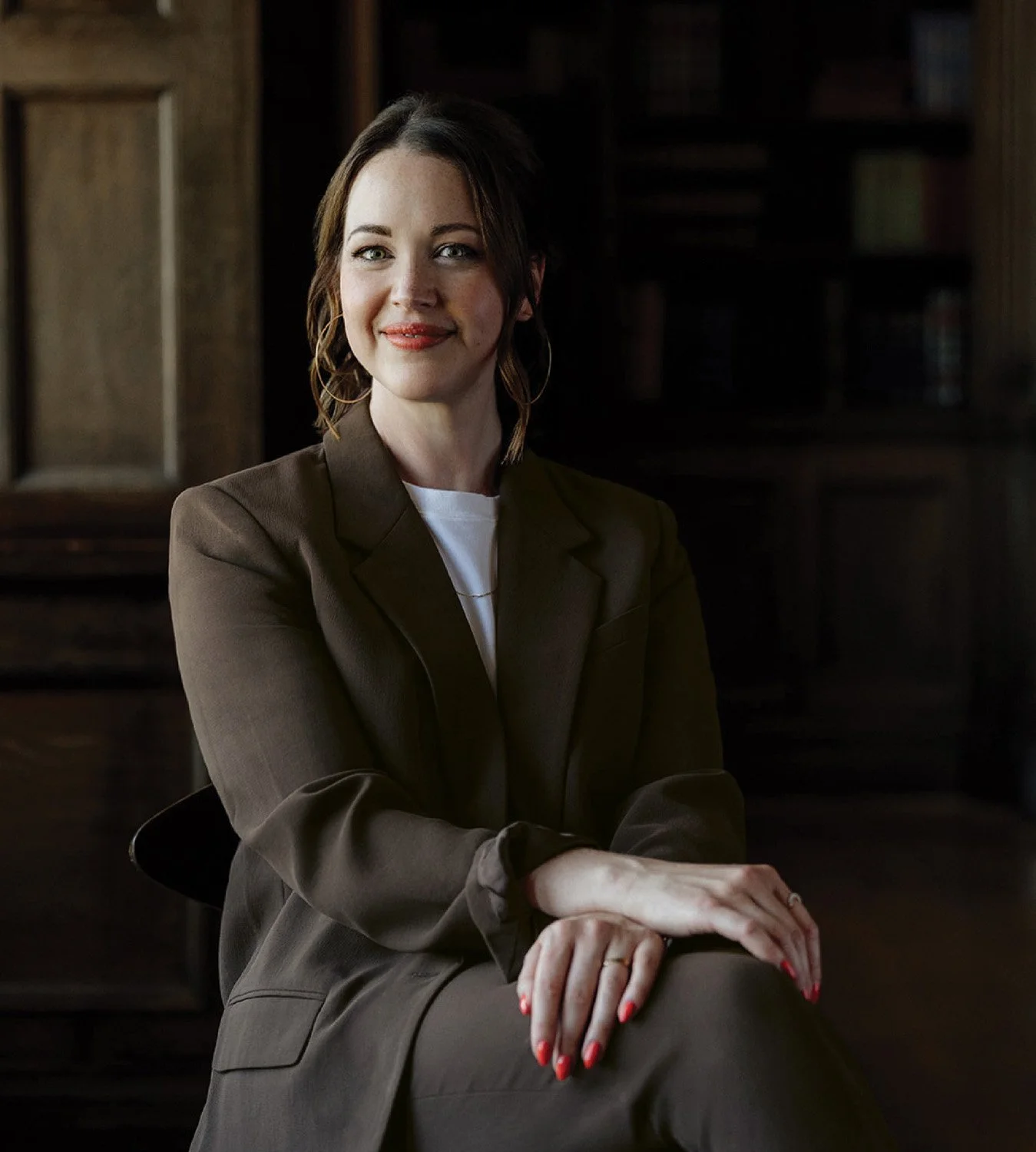 Jennifer Turner seated in a dark library wearing a brown suit for Gemini Copy Co’s editorial brand photoshoot