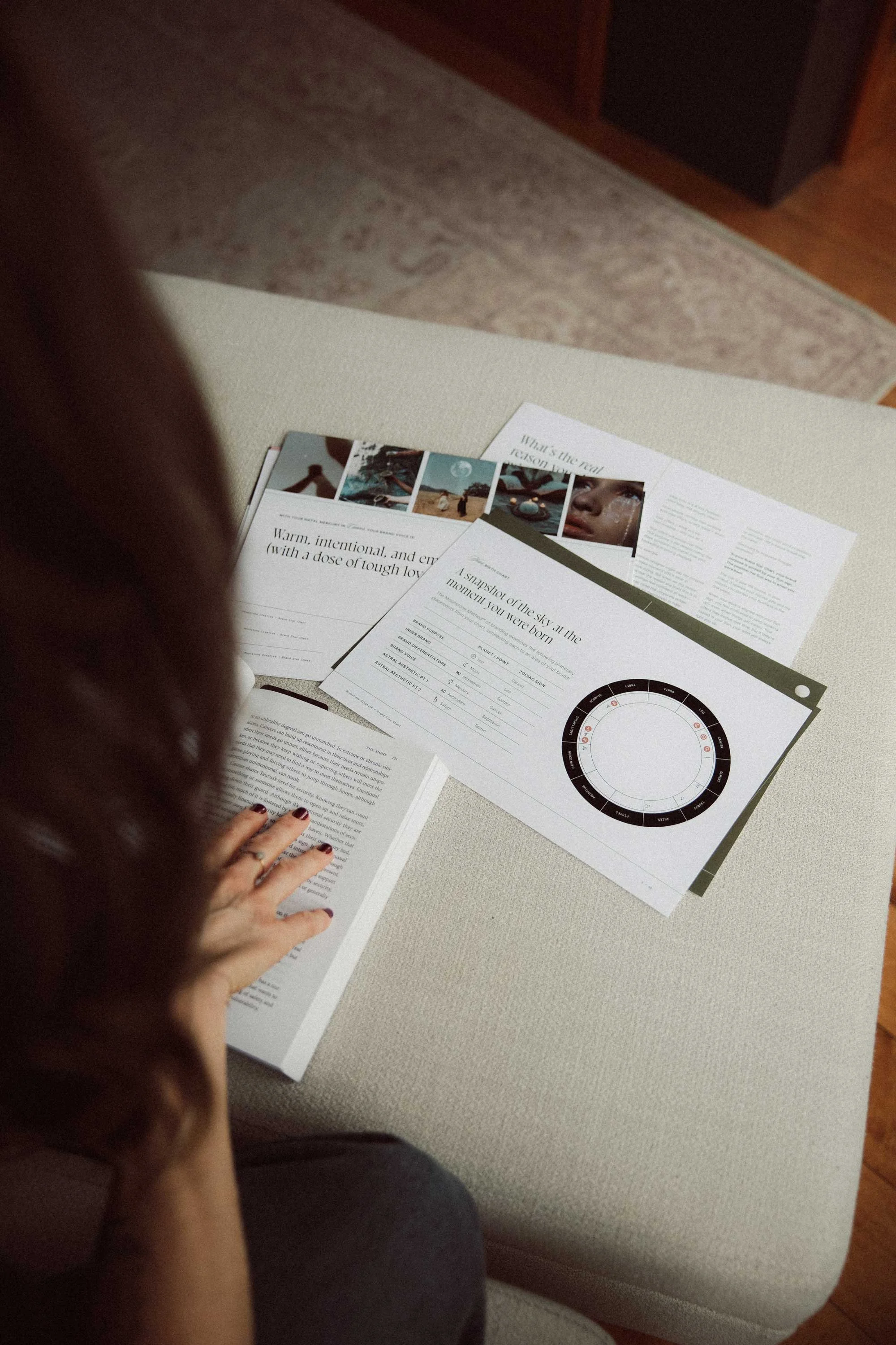 Moonstone Creative Brand Star Chart documents spread across a white ottoman including a natal chart wheel and brand positioning pages alongside an open book
