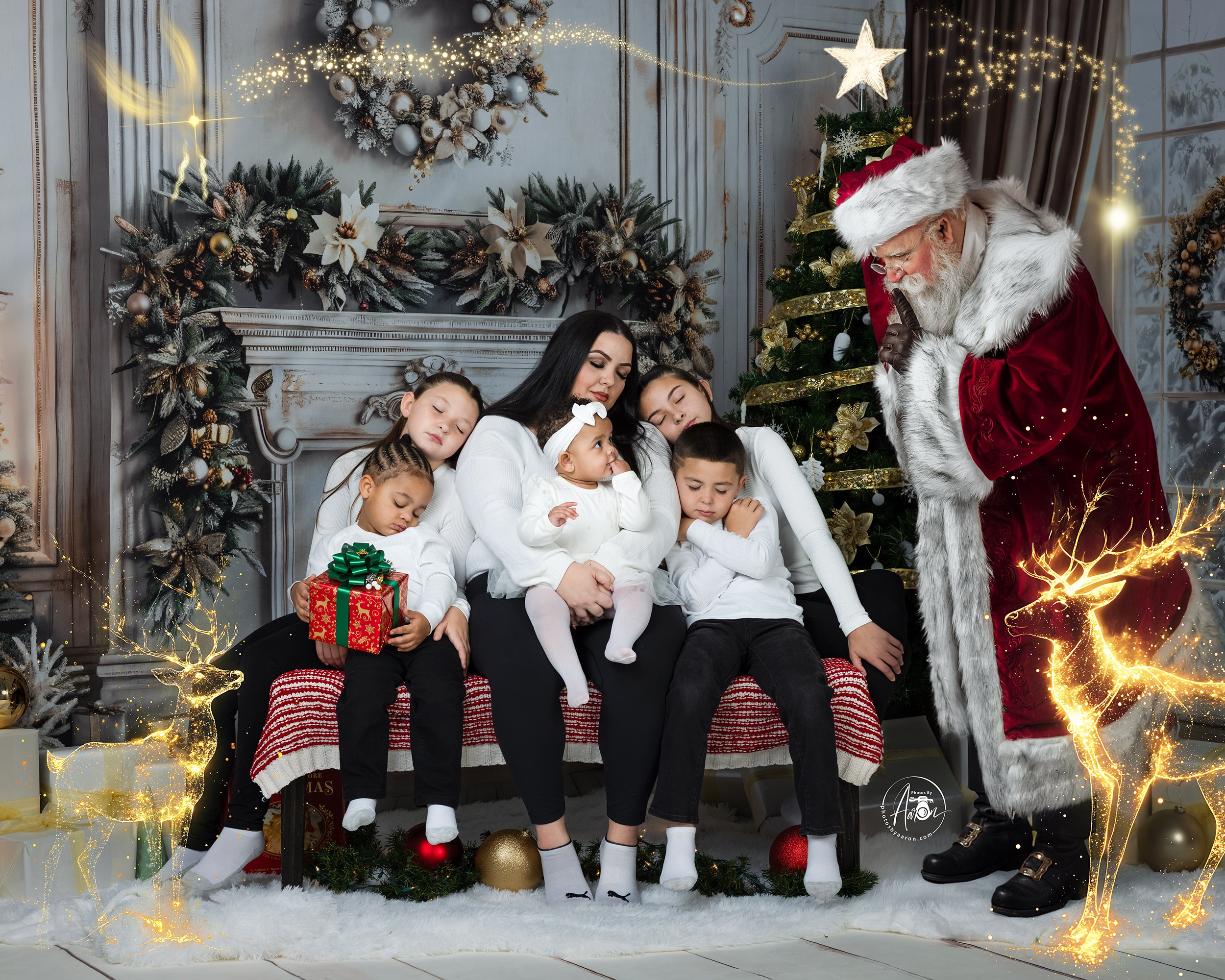 A young boy sitting on a fluffy white rug, opening a golden Christmas gift box. The background includes a fireplace, stockings, and holiday decorations, with a filter of sparkles and glowing hearts around him.