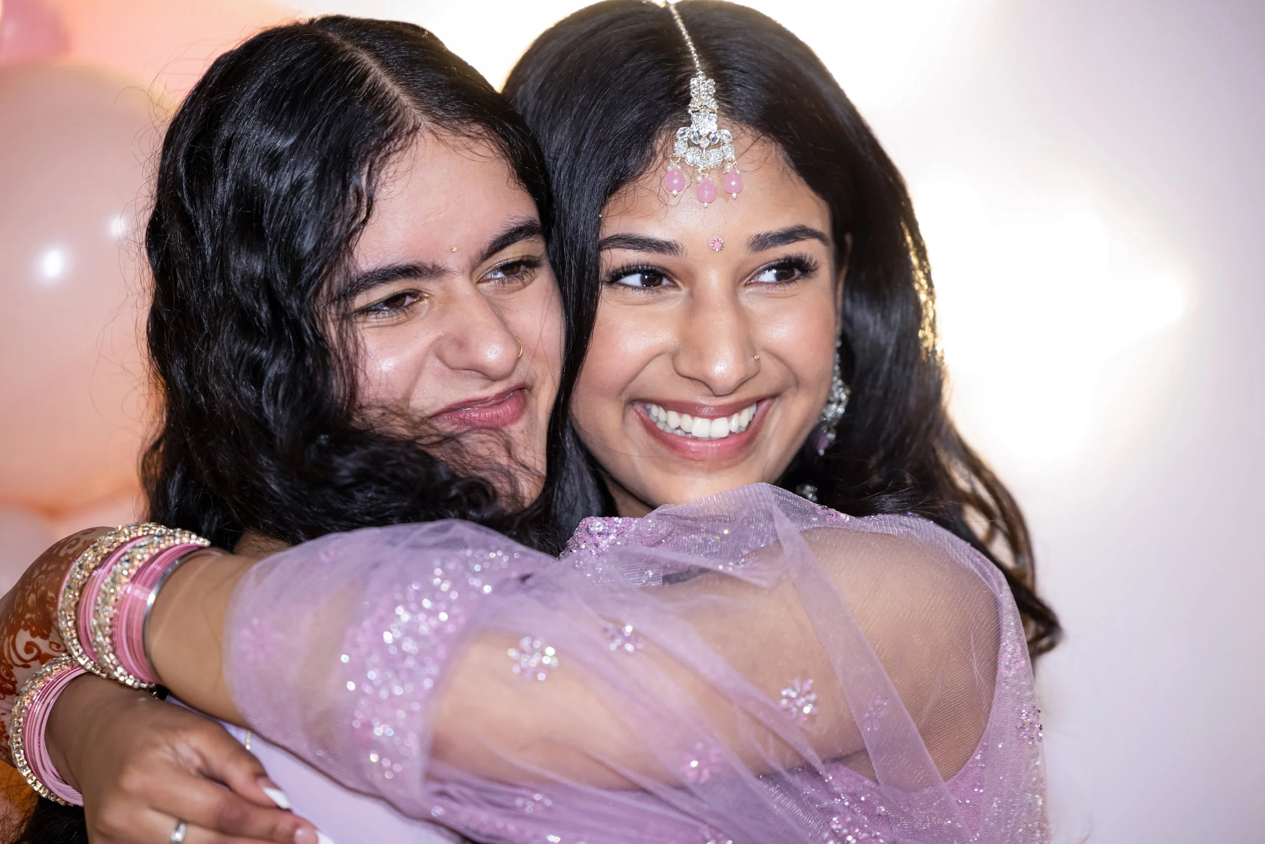 Two women in traditional Indian attire enjoying a celebration, with one woman applying henna on the other.
