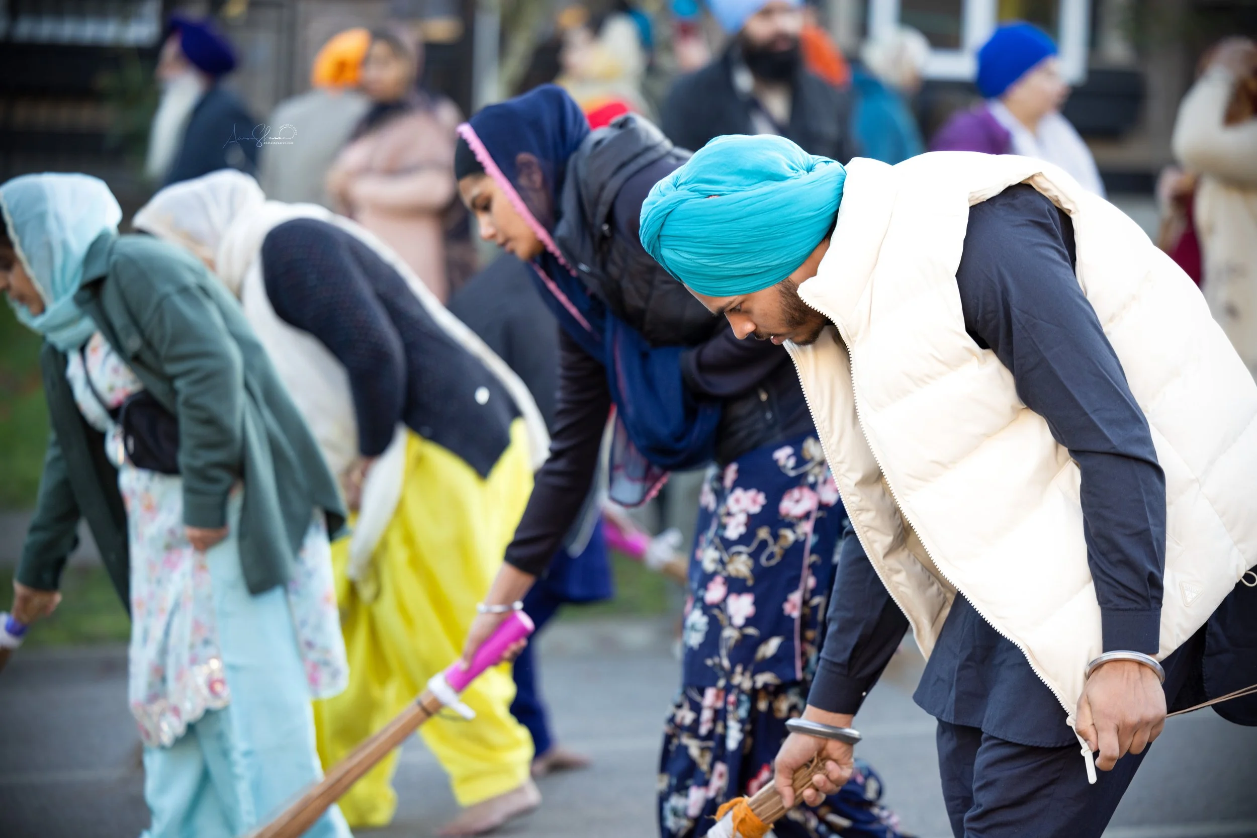 Group of people wearing traditional Sikh turbans and clothing, participating in a community event or prayer outdoors.