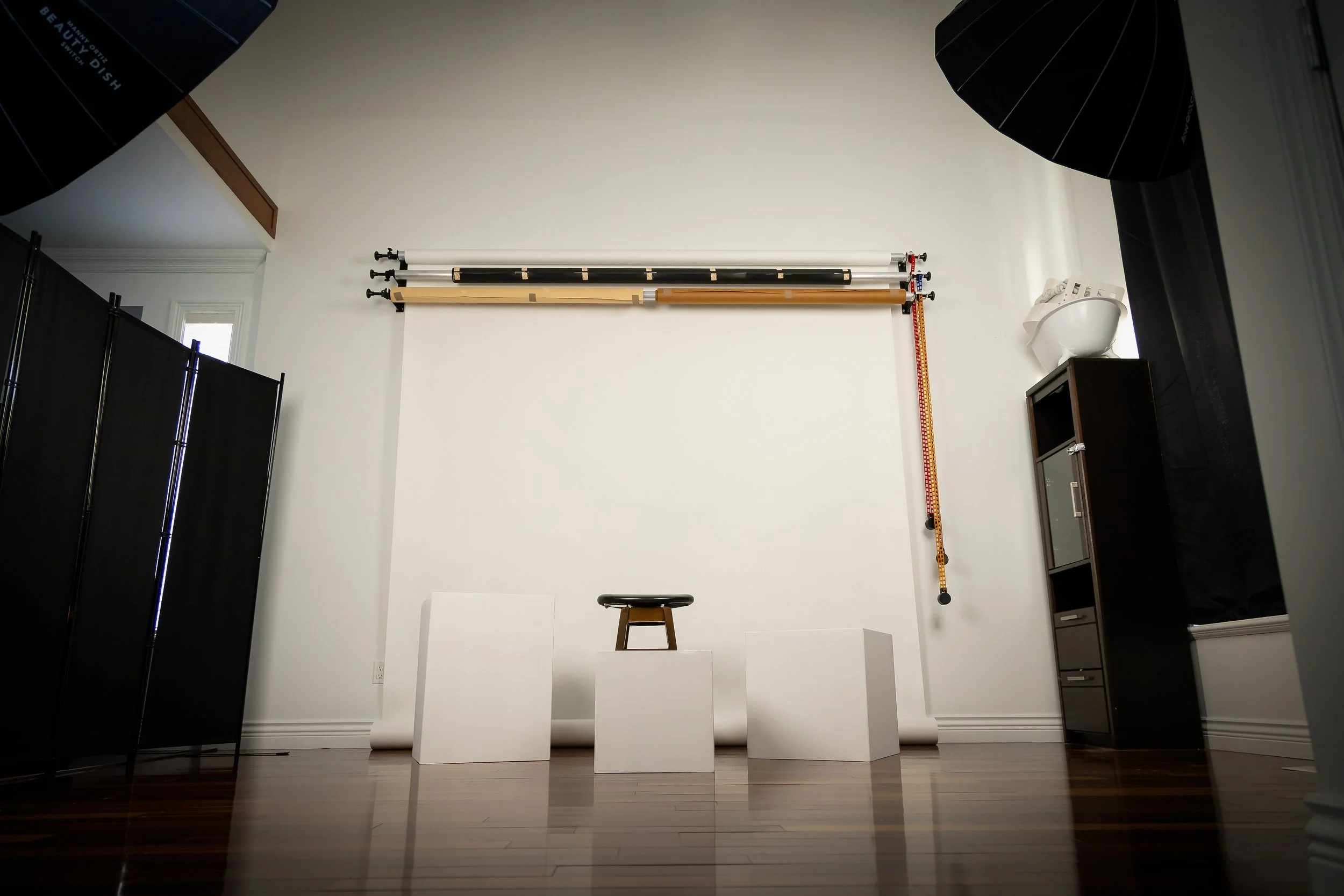 Photography studio with three white cubes, a stool, backdrop rails with backdrops, and black curtains with studio lights.