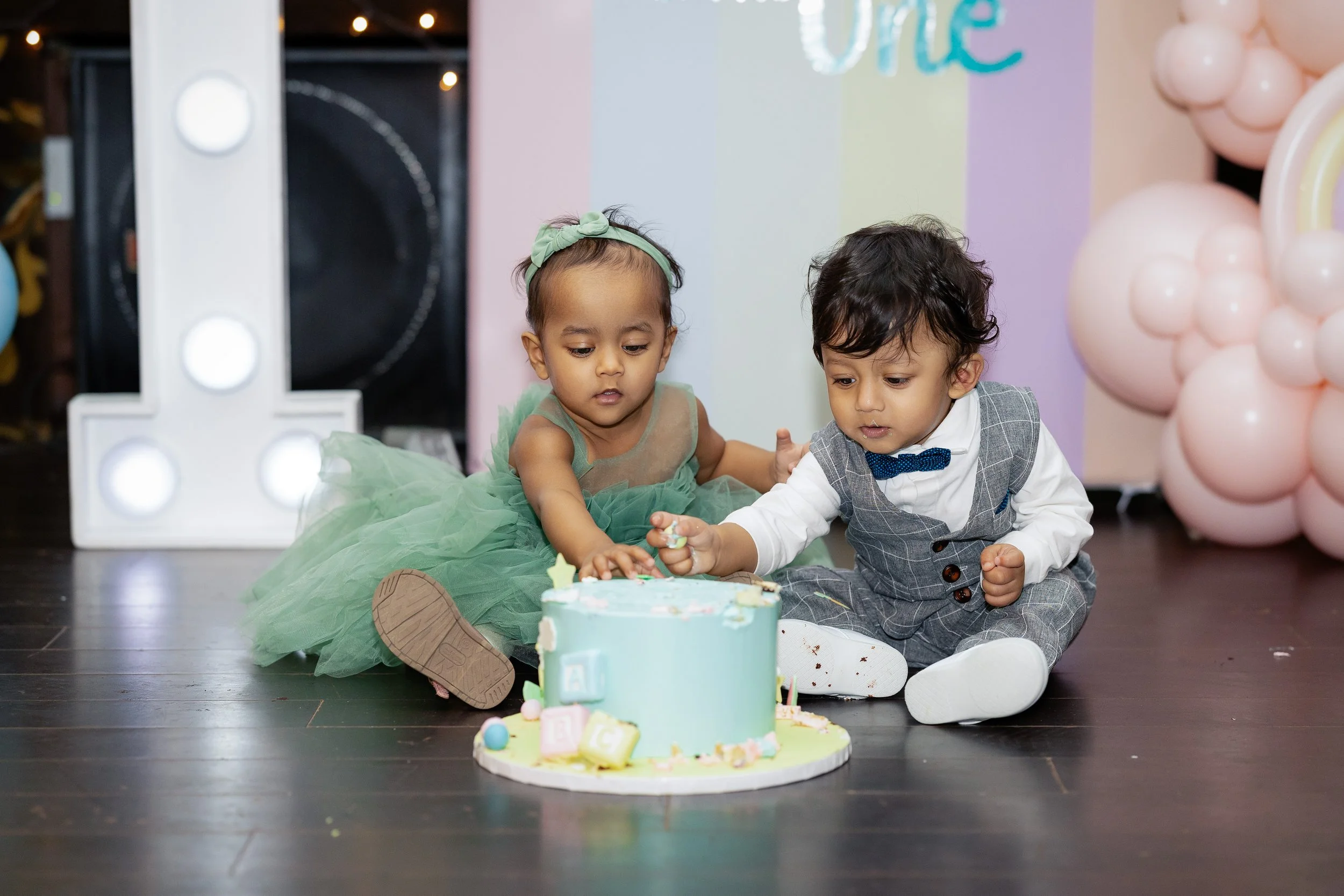 Family gathered around a birthday cake with colorful decorations and balloons, celebrating a child's first birthday.