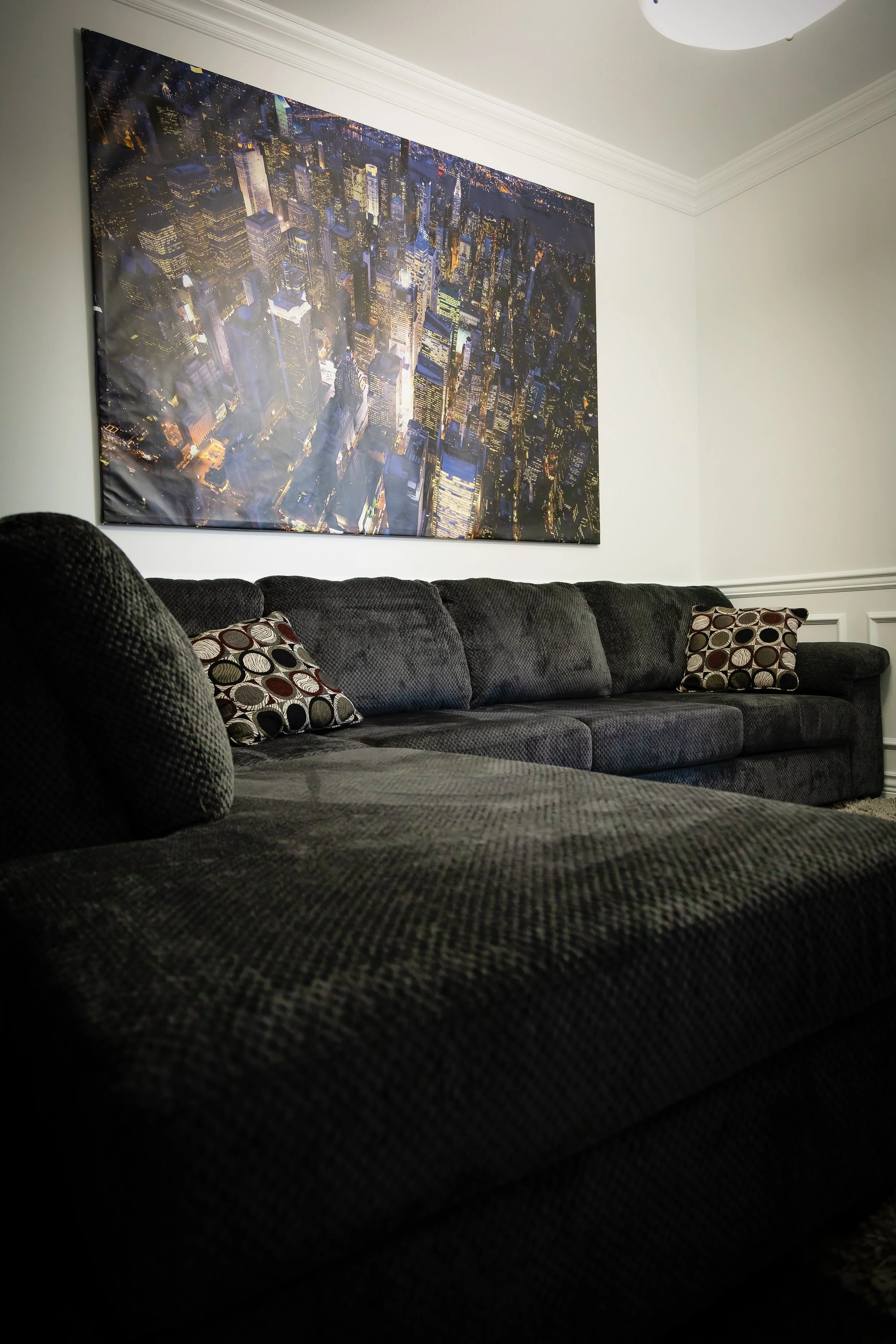 Living room with a dark gray couch, decorative pillows, and large cityscape artwork on the wall.
