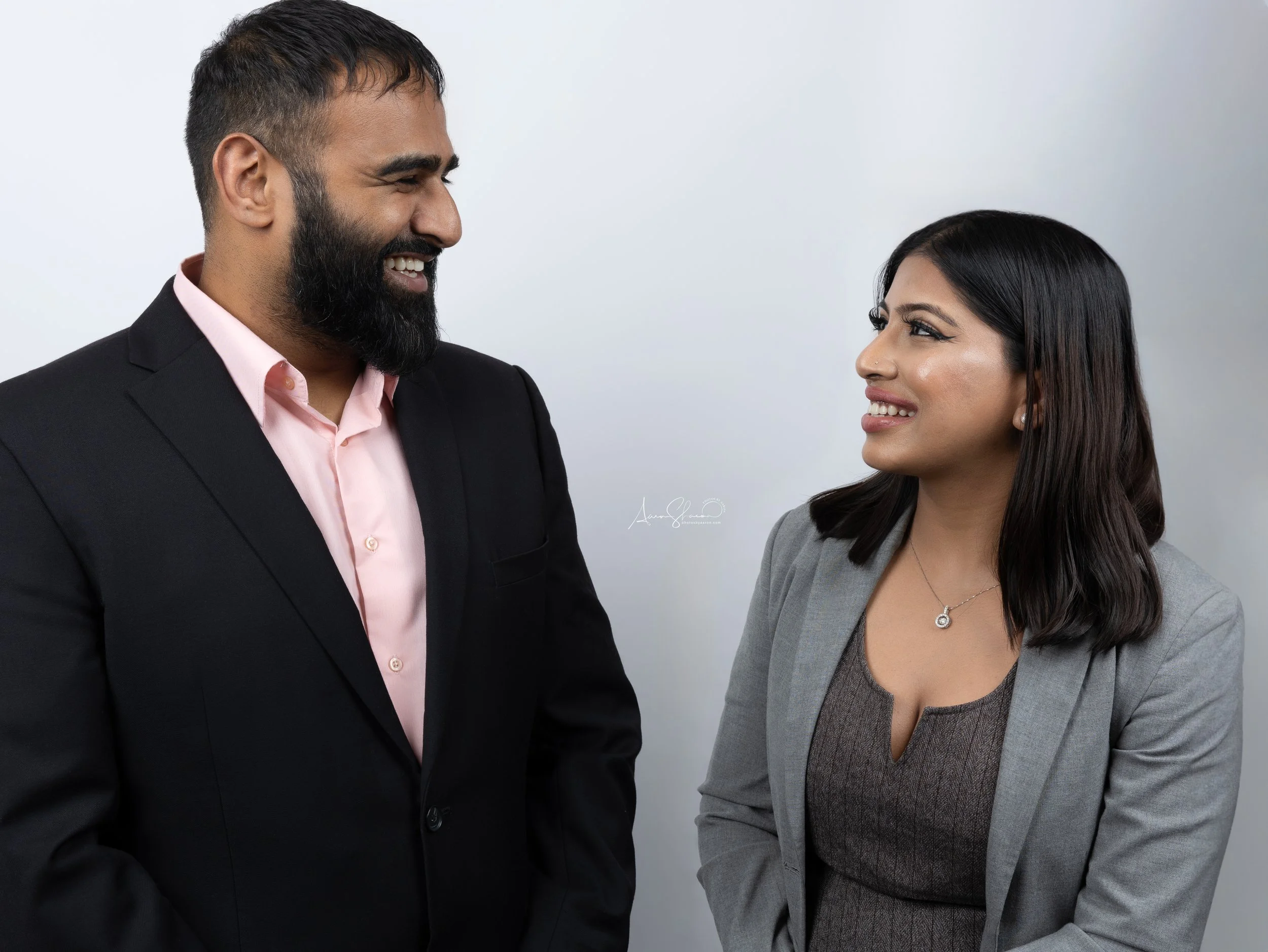 Two professionals, a man and a woman, smiling and looking at each other in a professional setting.