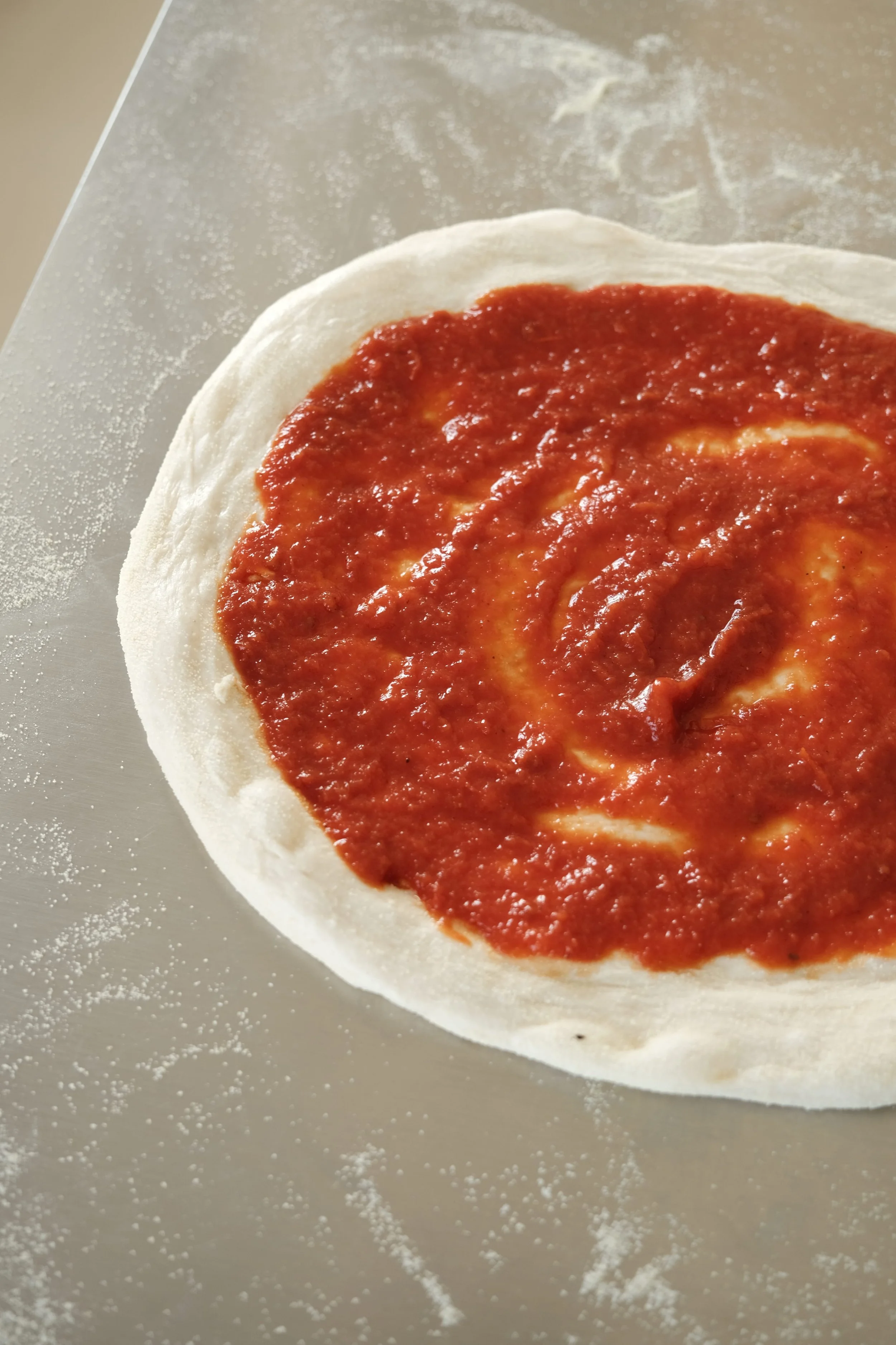 Pâte à pizza étalée et garnie de sauce tomate San Marzano lors de notre atelier à Nantes.