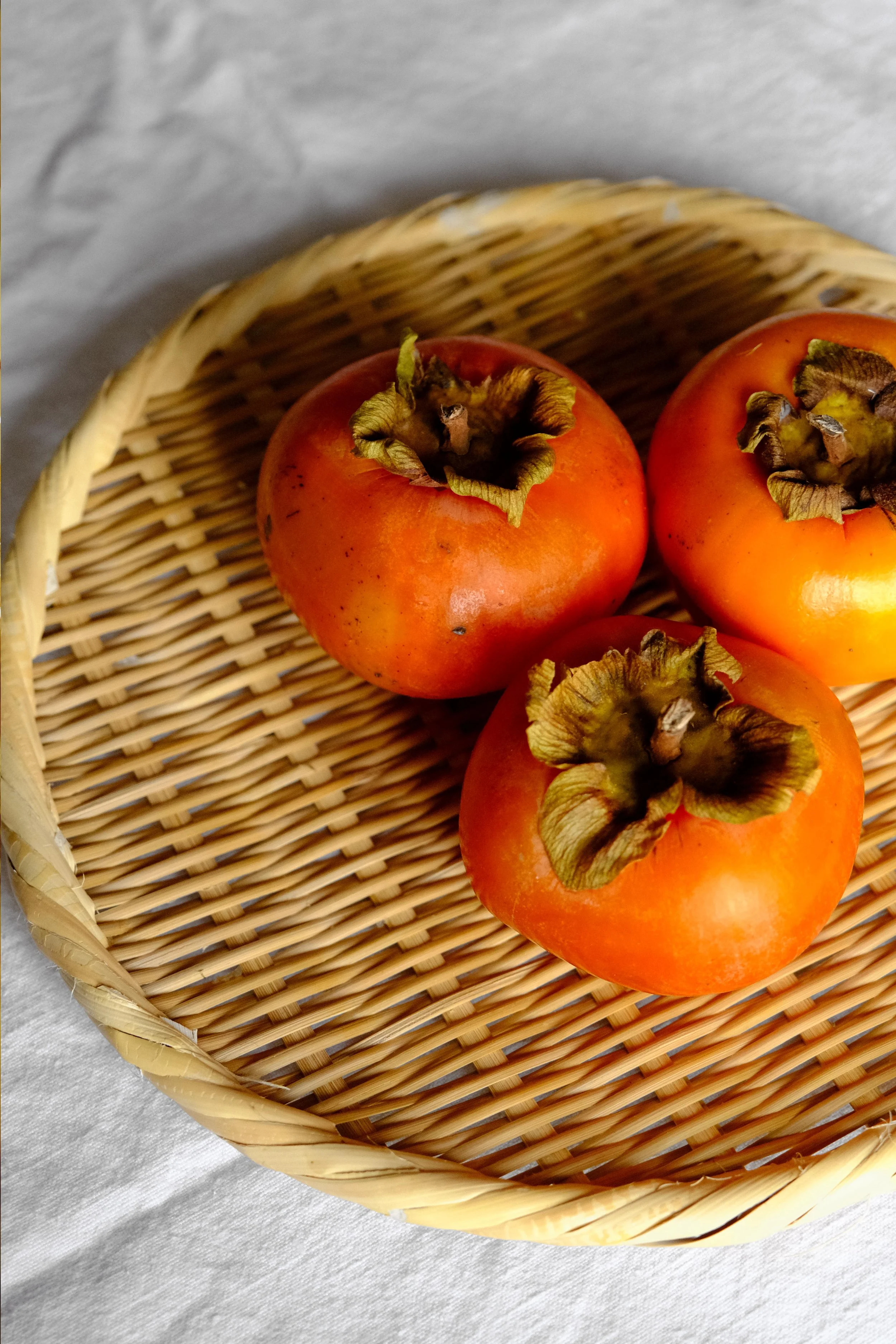 Trois kakis posées sur un plateau en osier. Ils sont suffisamment mûrs pour être utilisés dans un tajine avec du poulet. Gorgés de sucre ils apporteront beaucoup de douceur à notre plat salé.