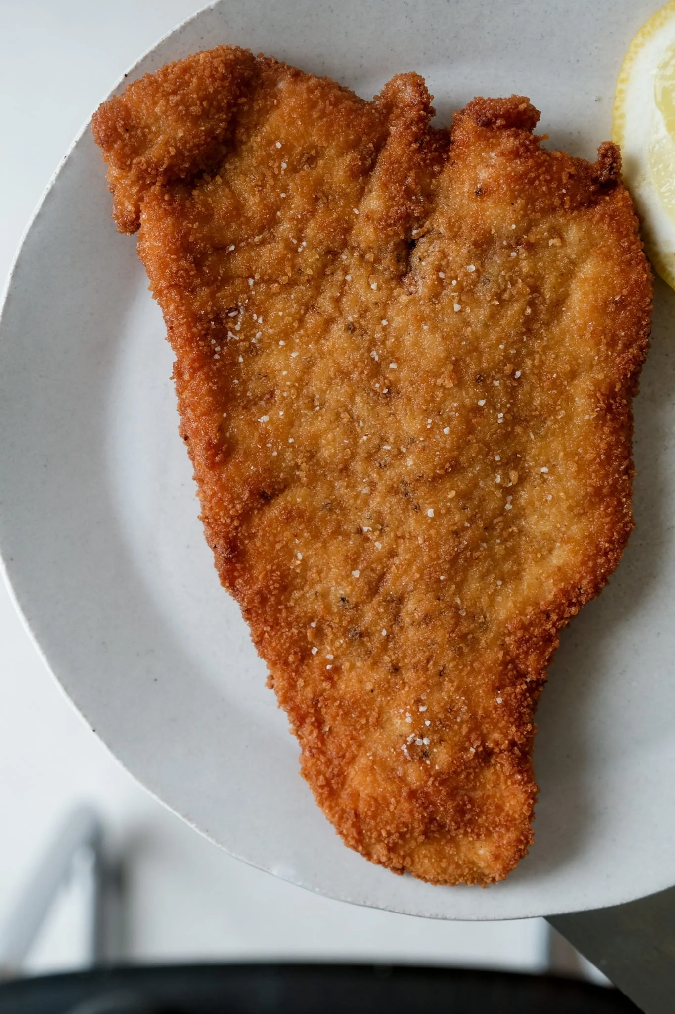 Plan rapproché d'une escalope panée façon viennoise dressée sur assiette, révélant la texture aérienne de sa croûte soufflée et ultra-croustillante.