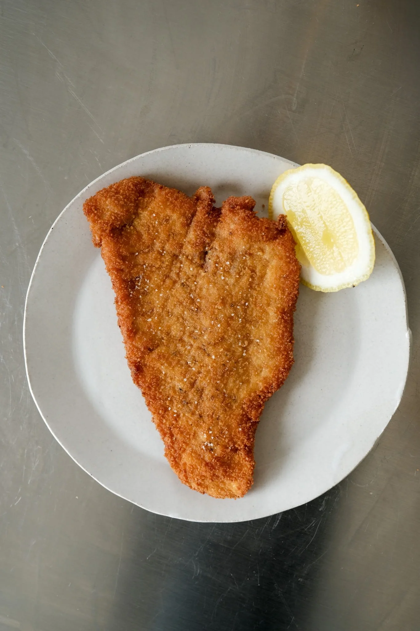 Vue de dessus d'un schnitzel de dinde parfaitement doré servi sur son assiette, accompagné de son traditionnel quartier de citron frais.