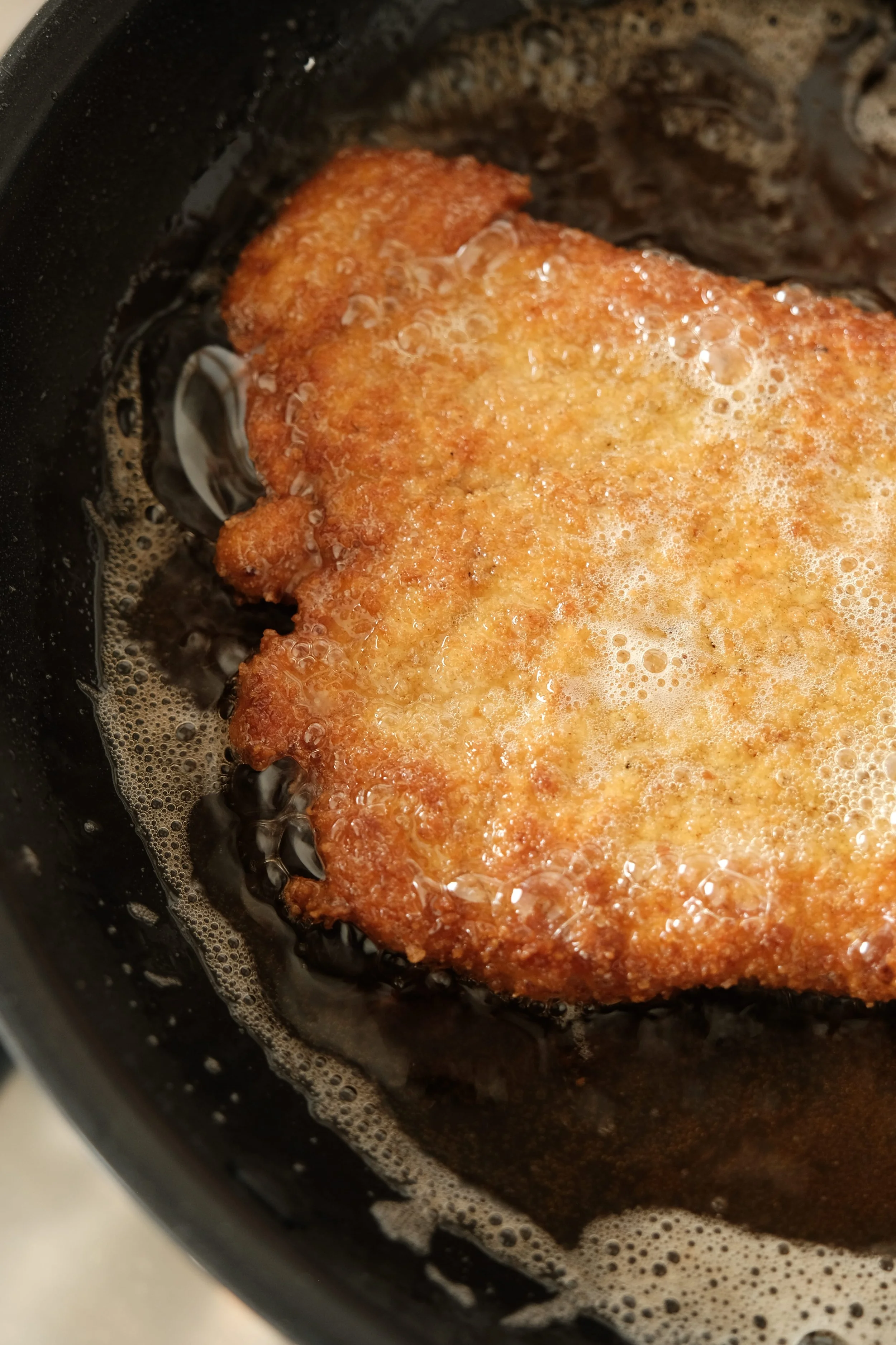 Cuisson d'un schnitzel de dinde à la poêle dans un beurre moussant pour obtenir l'authentique panure soufflée viennoise.