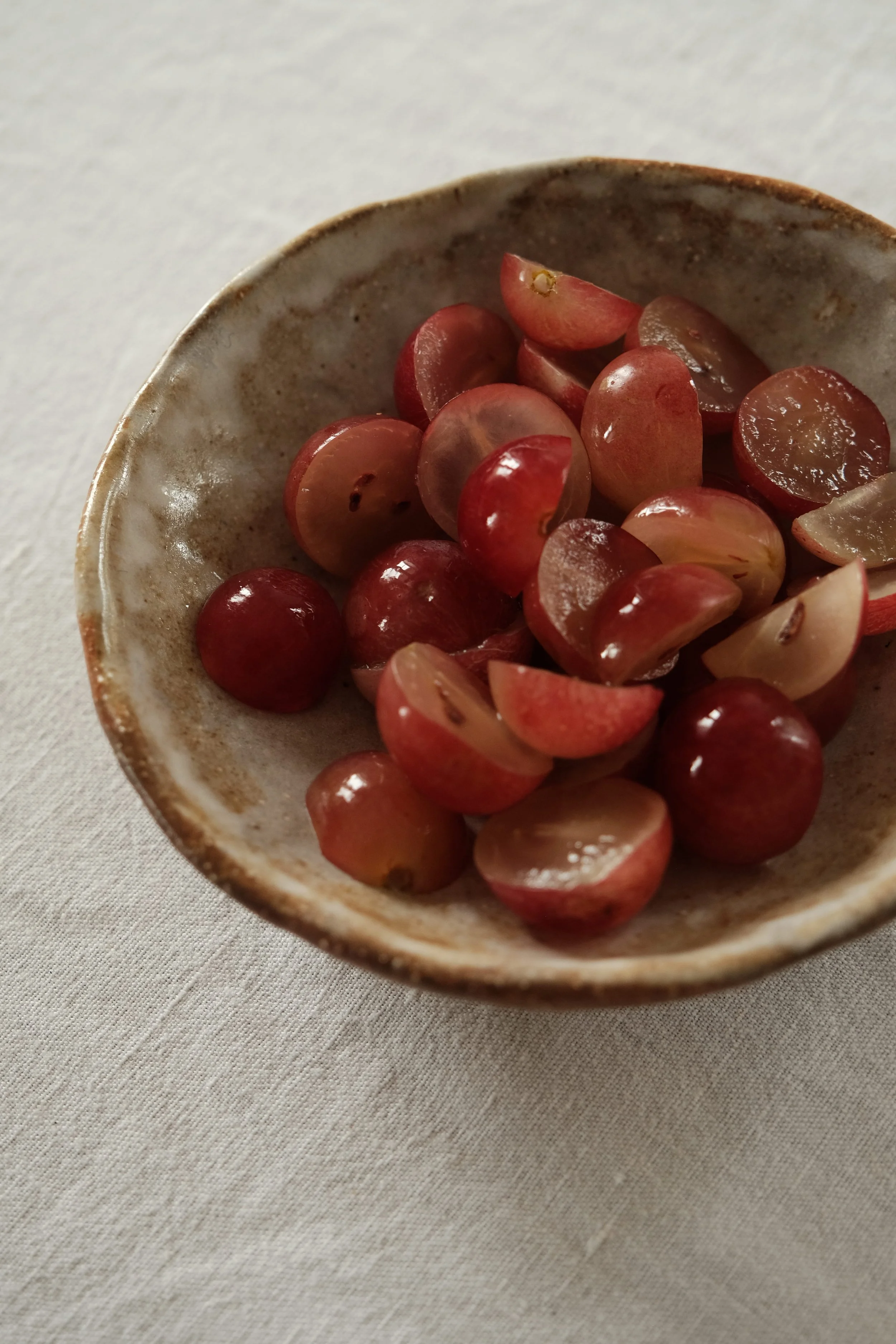 Préparation des ingrédients de la garniture du crudo : demi-raisins rouges, radis violet dégorgé et feuilles de shiso.