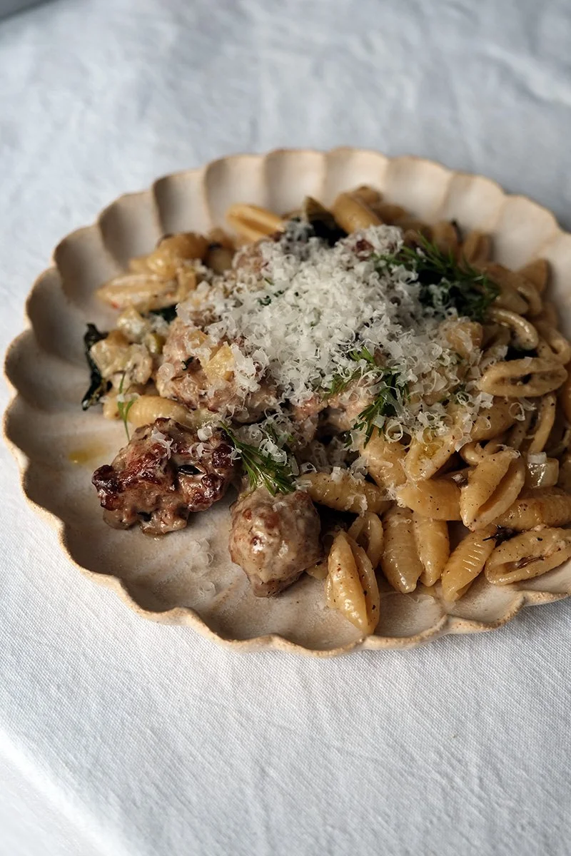 Assiette gnocchetti avec une sauce à base de crème, saucisse, chou khale et fenouil saupoudrée de parmesan. Présentée sur une nappe blanche.