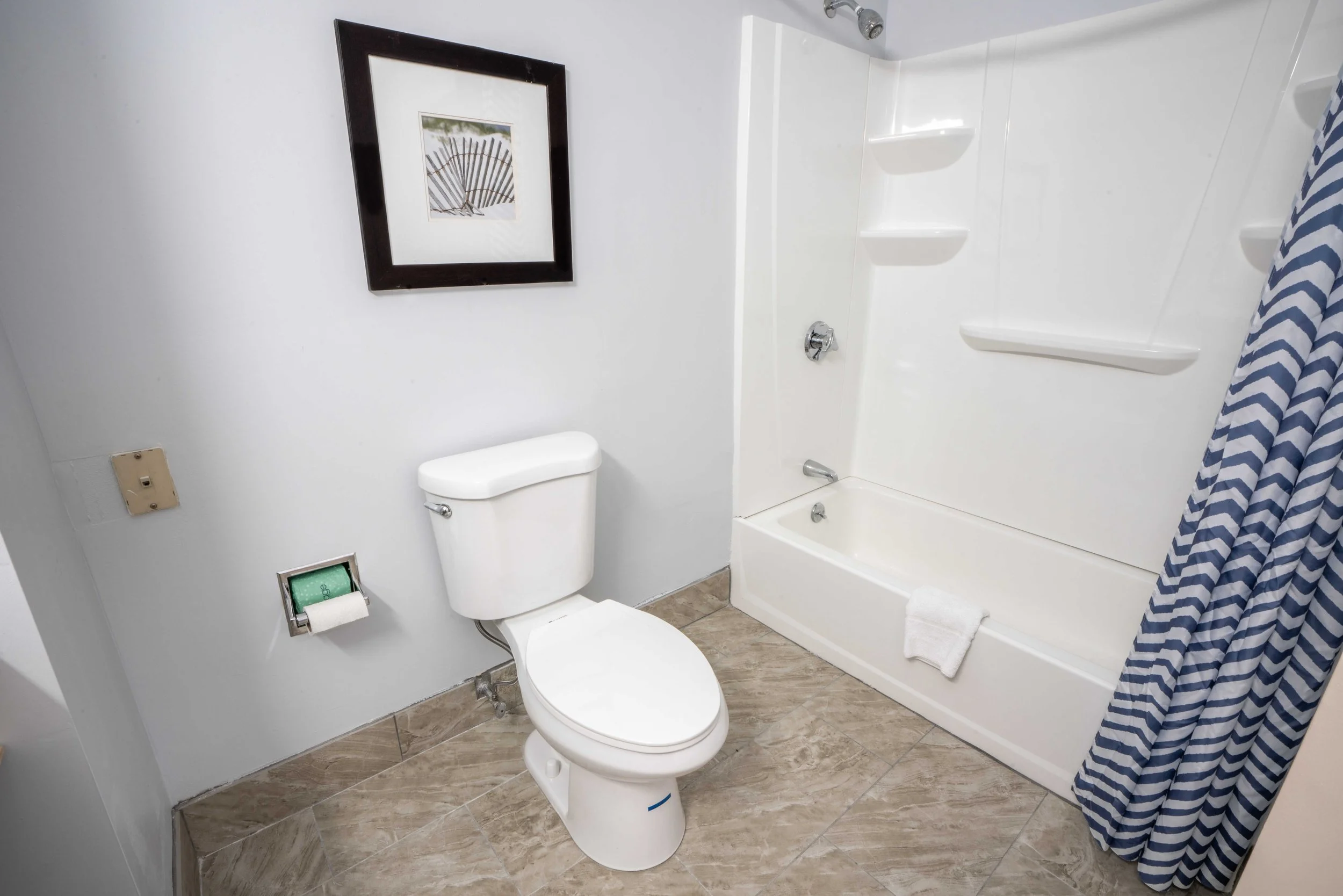 Bathroom with toilet, bathtub, shower curtain, wall art, and tile floor.
