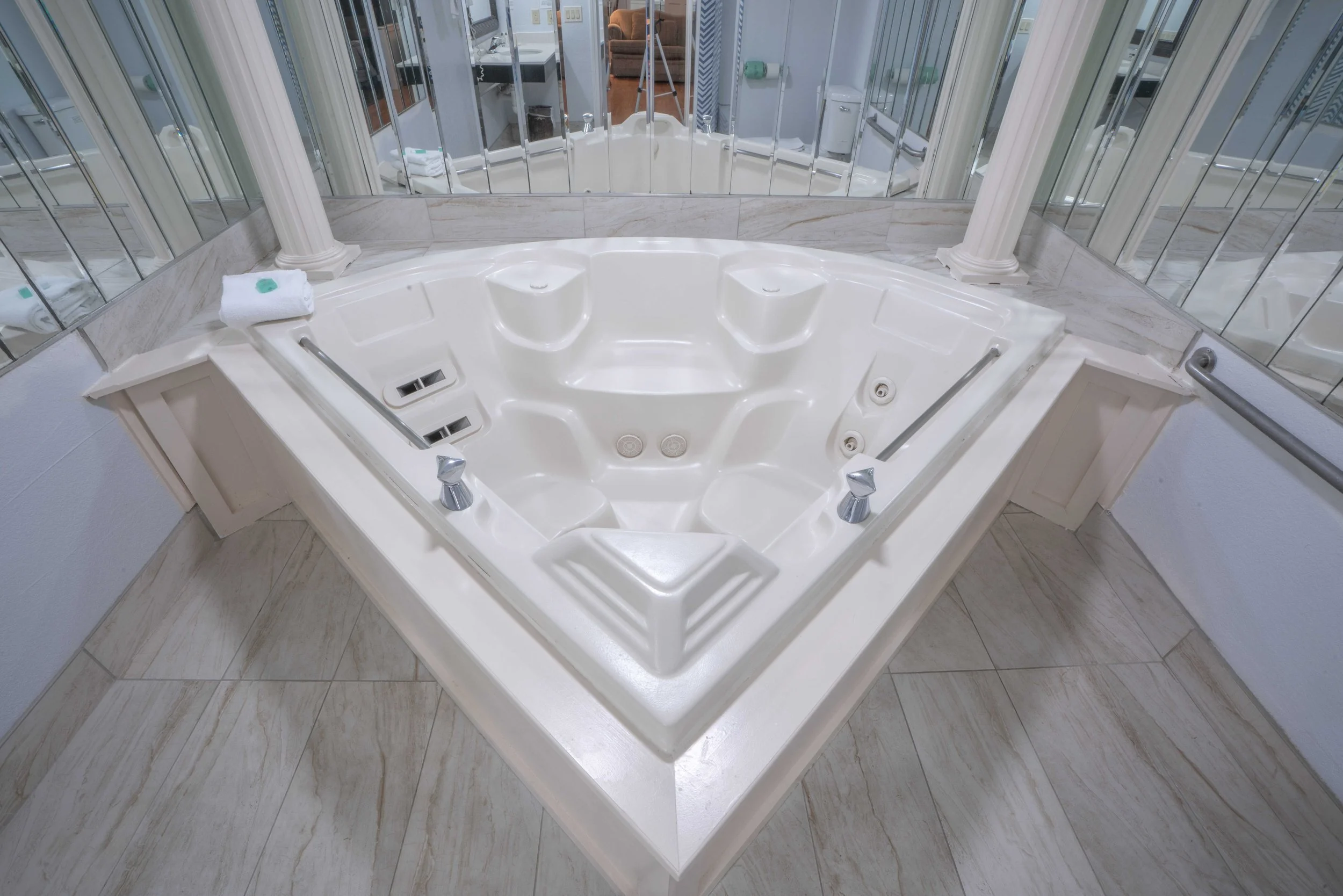Corner bathtub with jets and mirrors, featuring a towel on the edge in a bathroom setting.