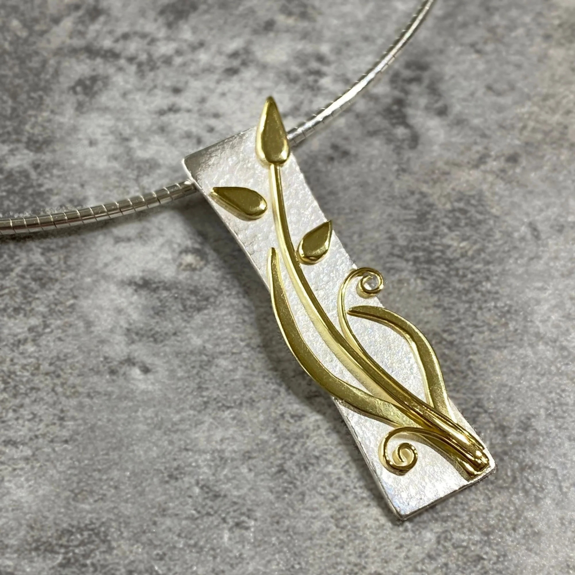 Long Silver Pendant with curled gold leaves and stylised flower buds