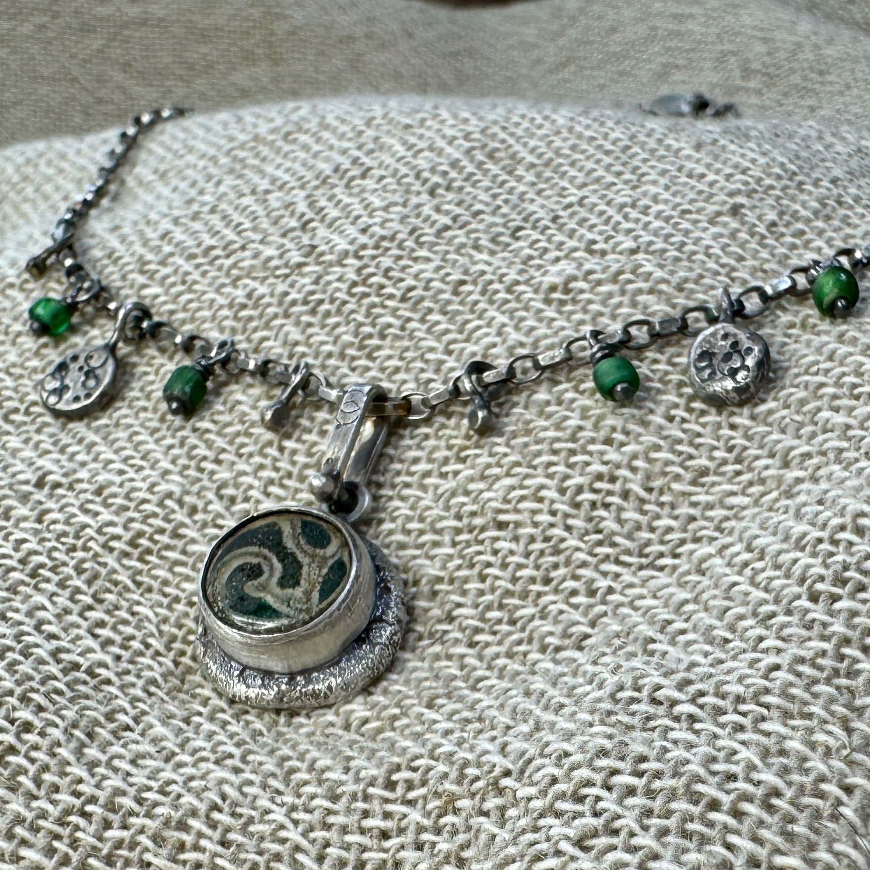 Close up of a swirl patterned glass pendant with small beads and charms on an oxidised chain