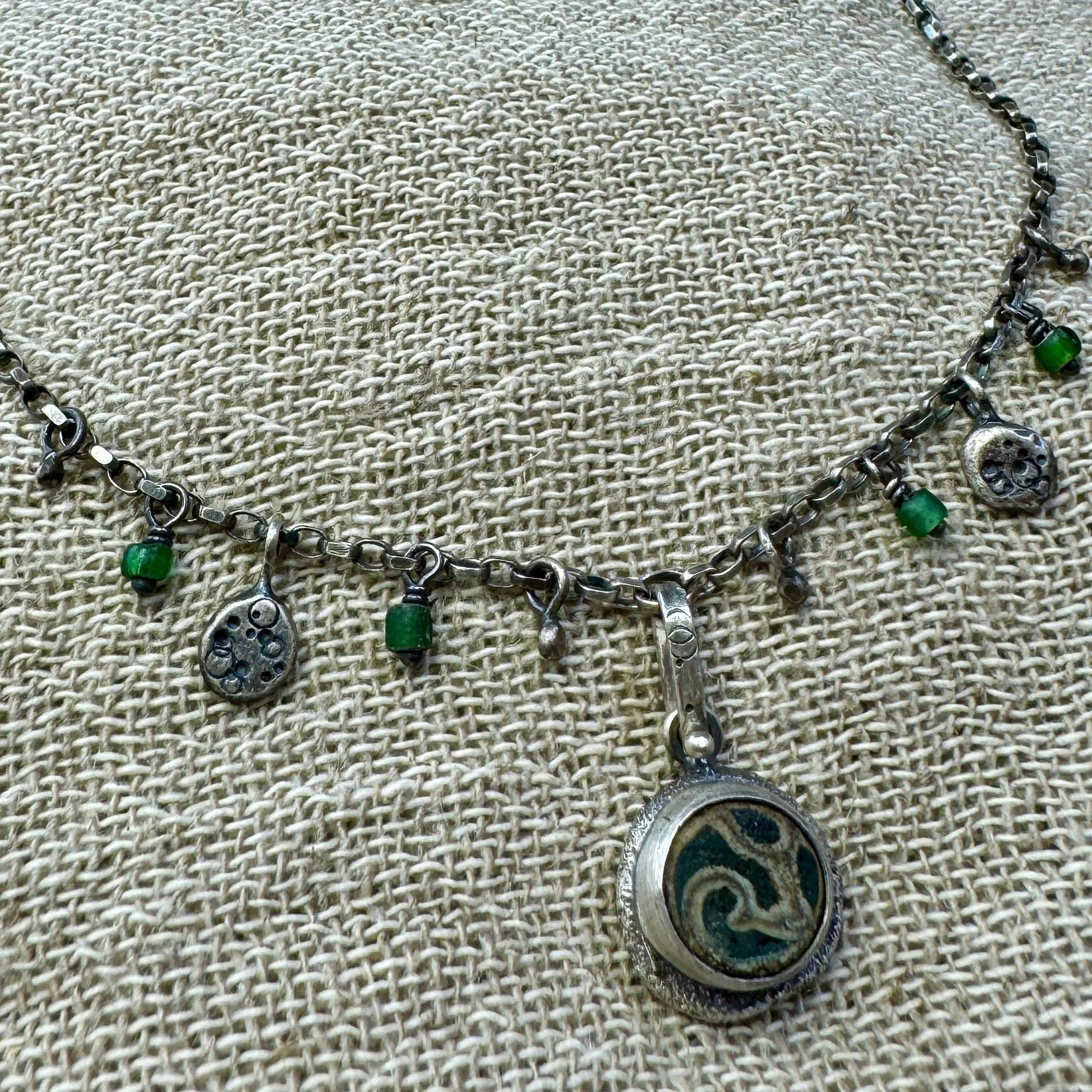 Swirl patterned turquoise glass pendant with small beads and charms on an oxidised chain