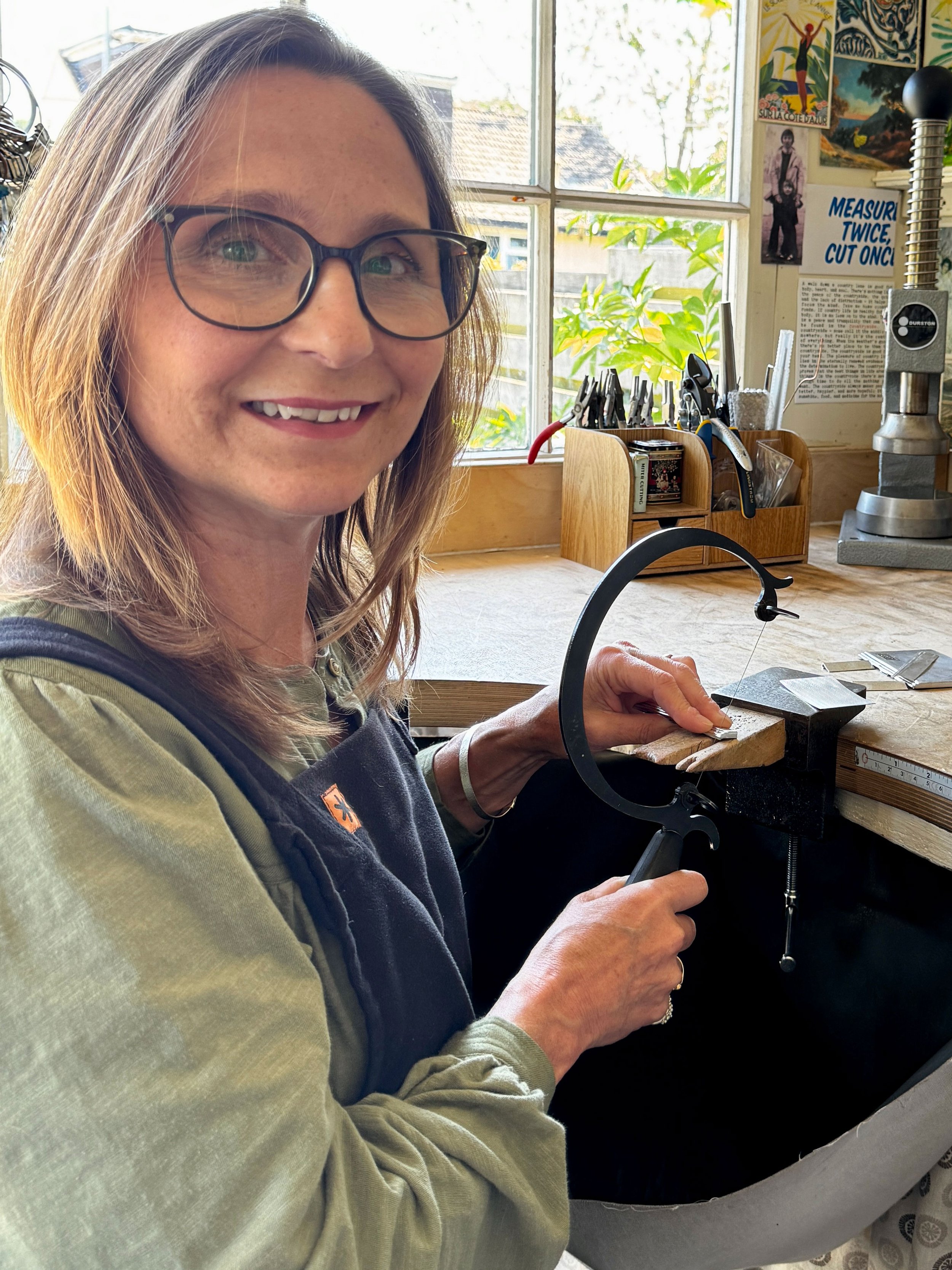 Charlotte at her bench using a piercing saw and looking at the camera