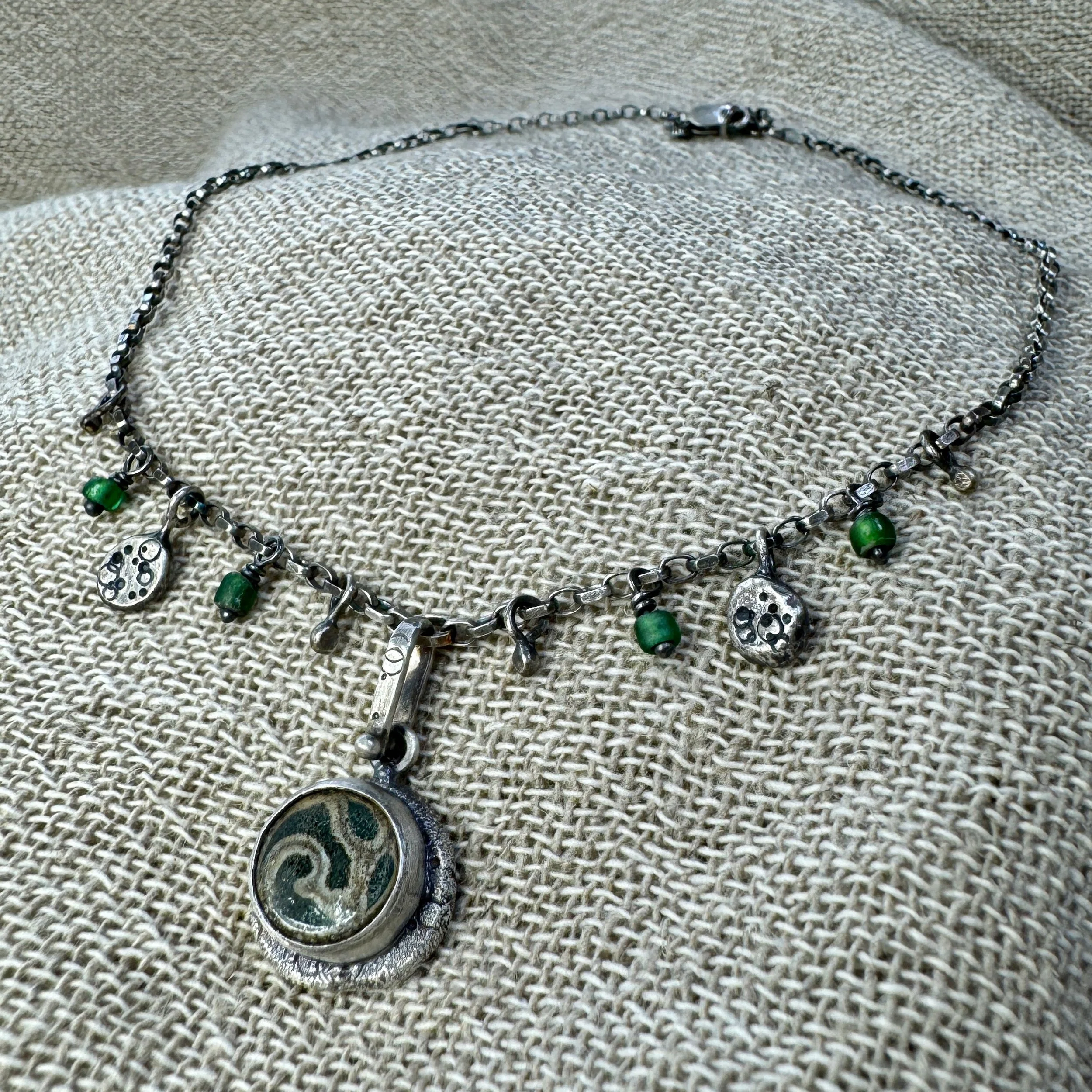Swirl patterned glass pendant with small beads and charms on an oxidised chain