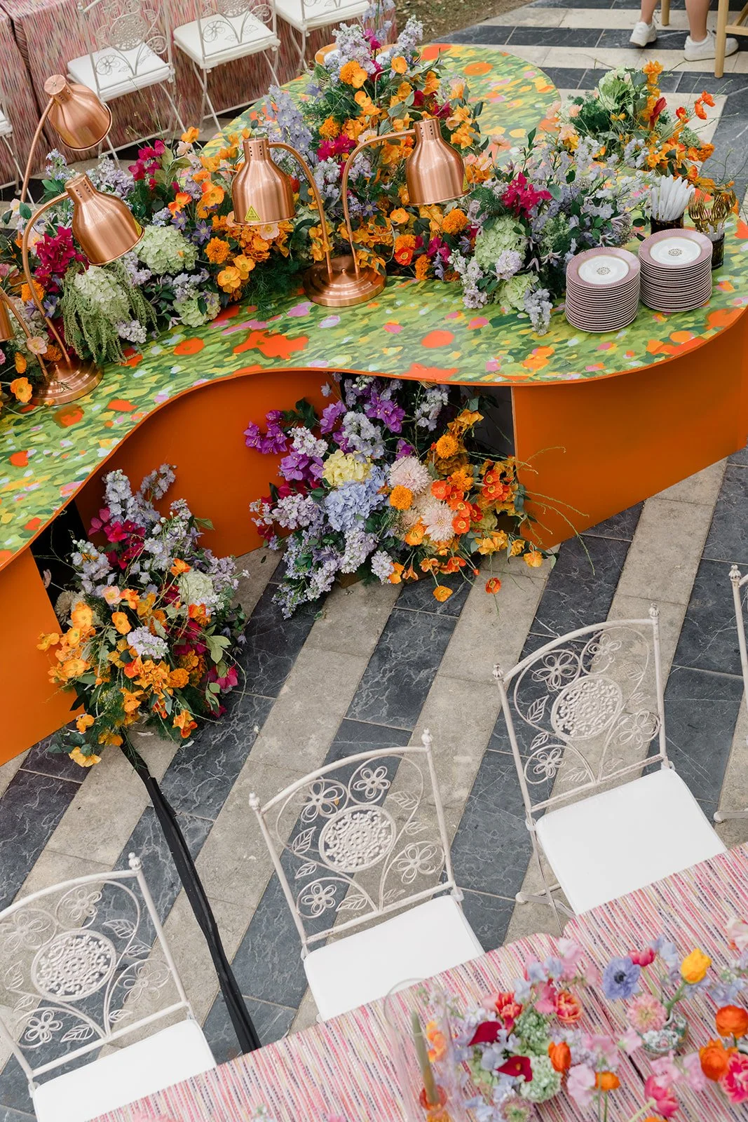  Curved patterned buffet counter with copper pendant lights and a colorful floral arrangement at Hotel St. Cecilia's reception 