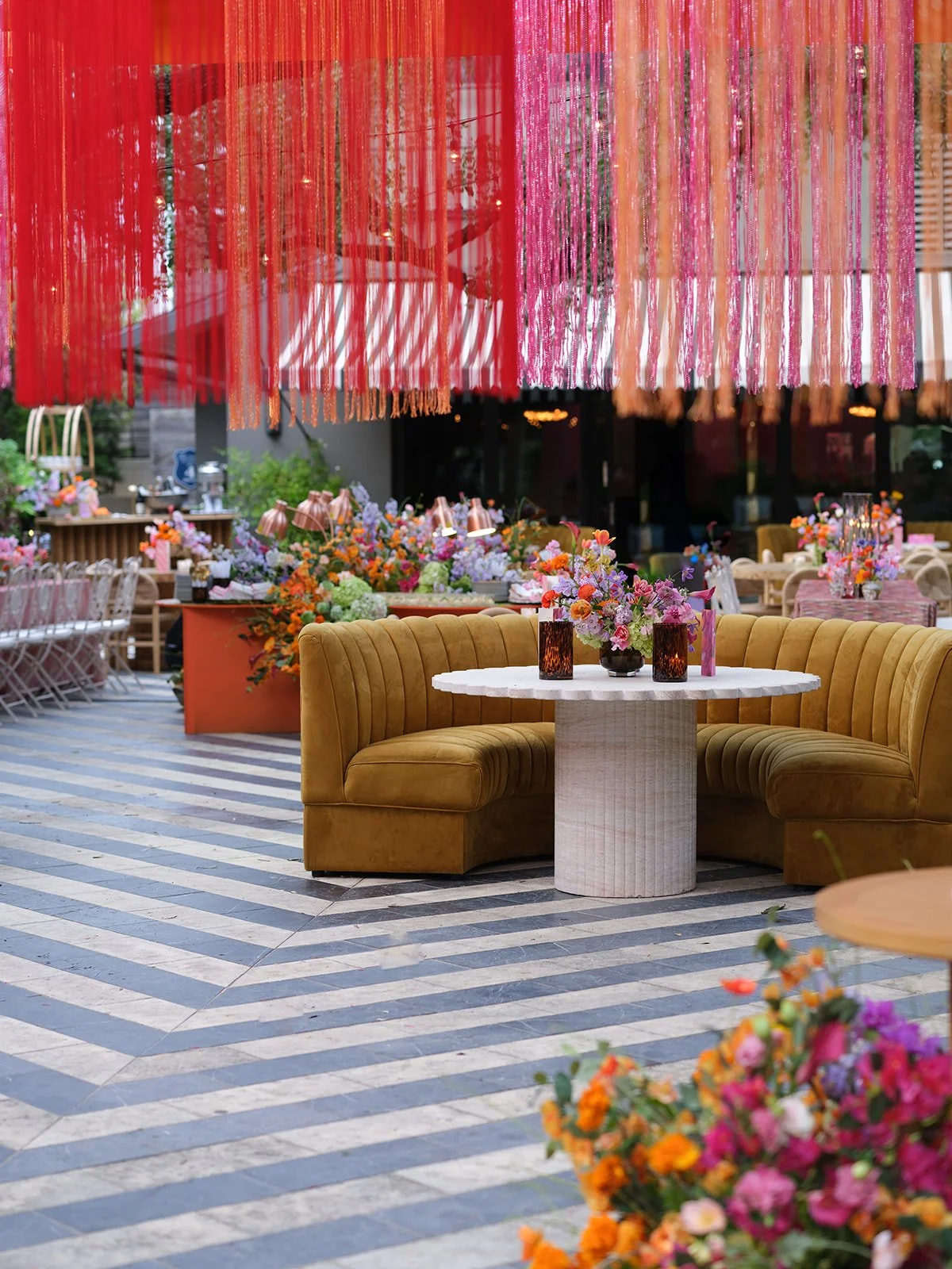  Mustard velvet banquette seating and a round scalloped table under hanging pink and orange fringe at a Hotel St. Cecilia wedding reception 