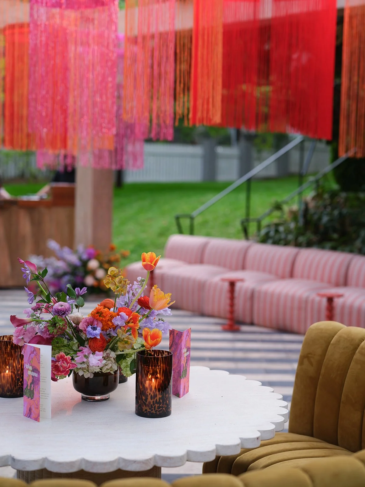  Pink and red fringe installation above a striped velvet lounge with a jewel-toned floral centerpiece at Hotel St. Cecilia 