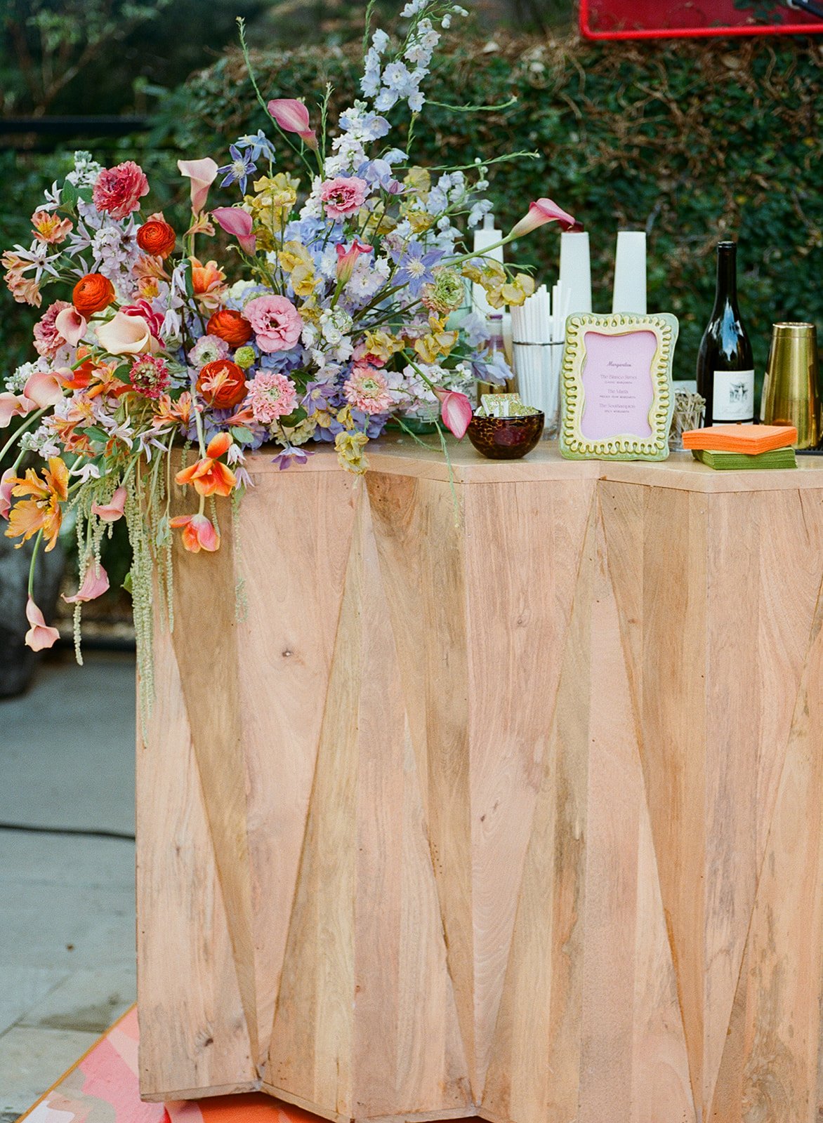 Diamond-paneled wooden bar with a cascading floral arrangement in red, pink, and purple at Hotel St. Cecilia 