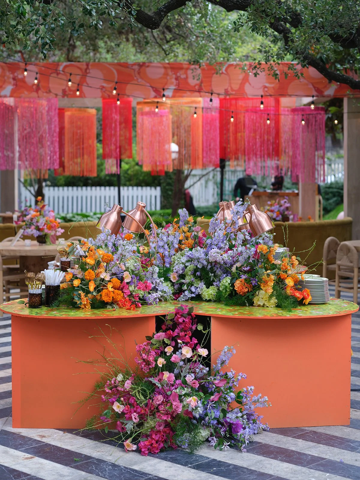 Orange and green curved buffet structure with abundant cascading florals beneath a hanging fringe installation at Hotel St. Cecilia 
