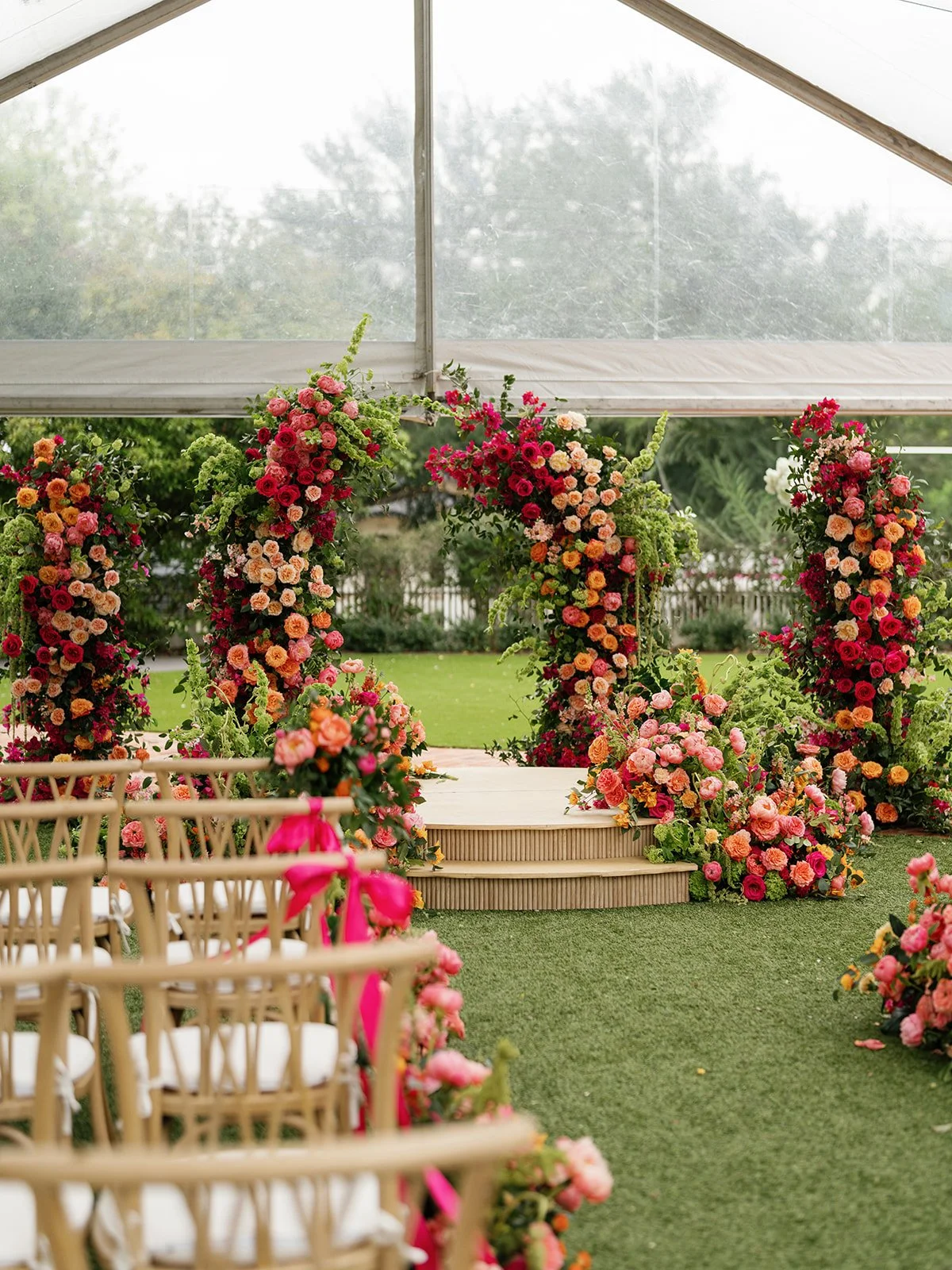  Close-up of the round floral ceremony arch in red, orange, and pink blooms with trailing greenery above the wooden steps at Woodbine Mansion 