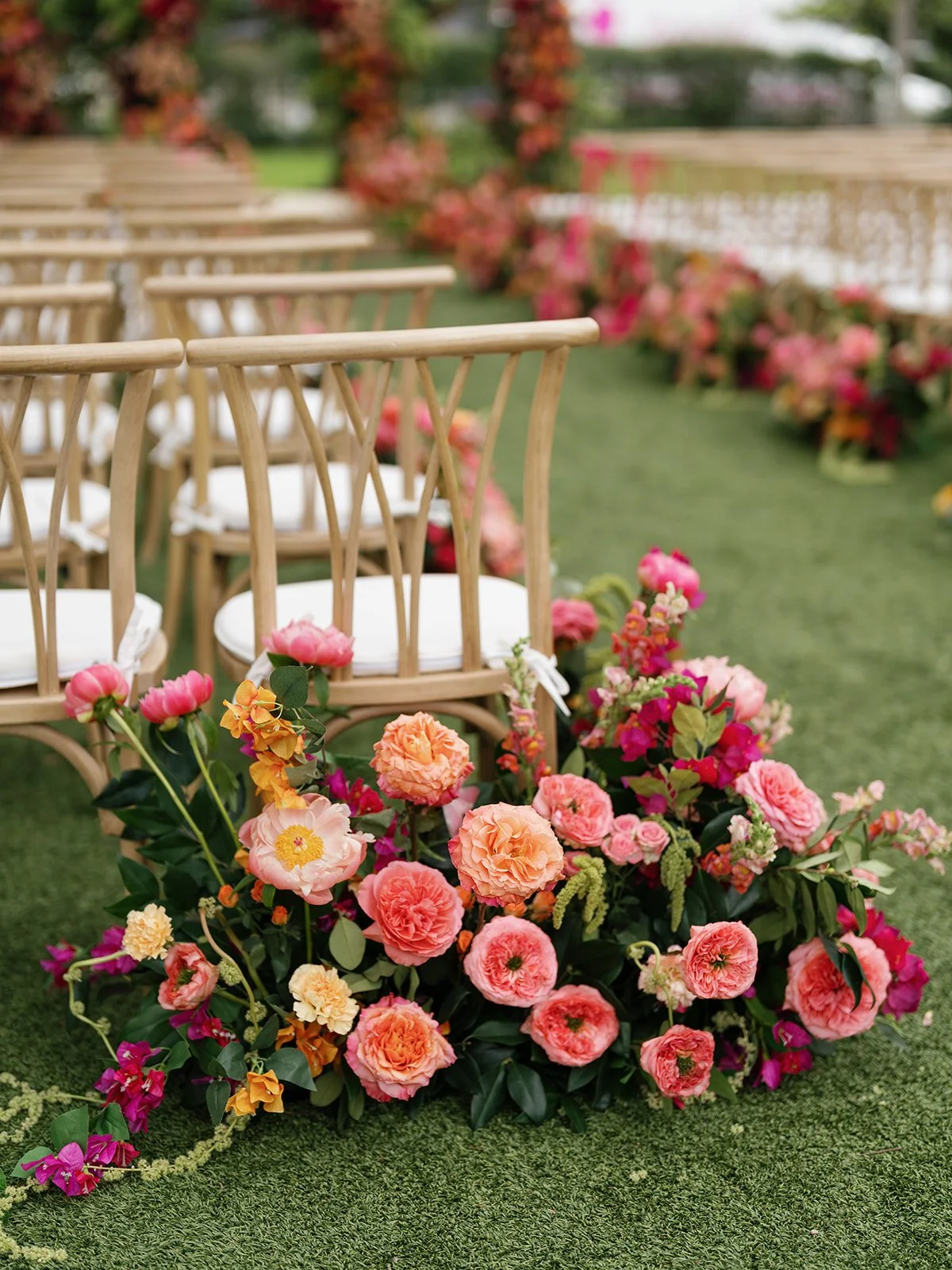  Cane-back ceremony chairs beside a lush aisle floral cluster in coral, pink, and yellow at Woodbine Mansion 