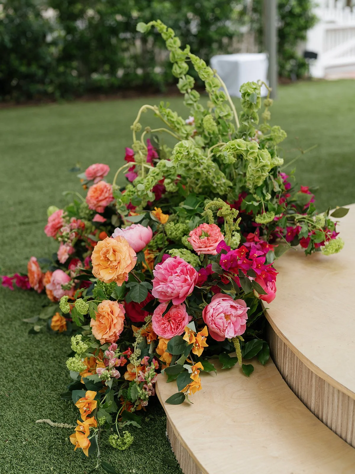  Close-up floral arrangement with garden roses, ranunculus, and trailing bells of Ireland at the base of the ceremony steps at Woodbine Mansion 