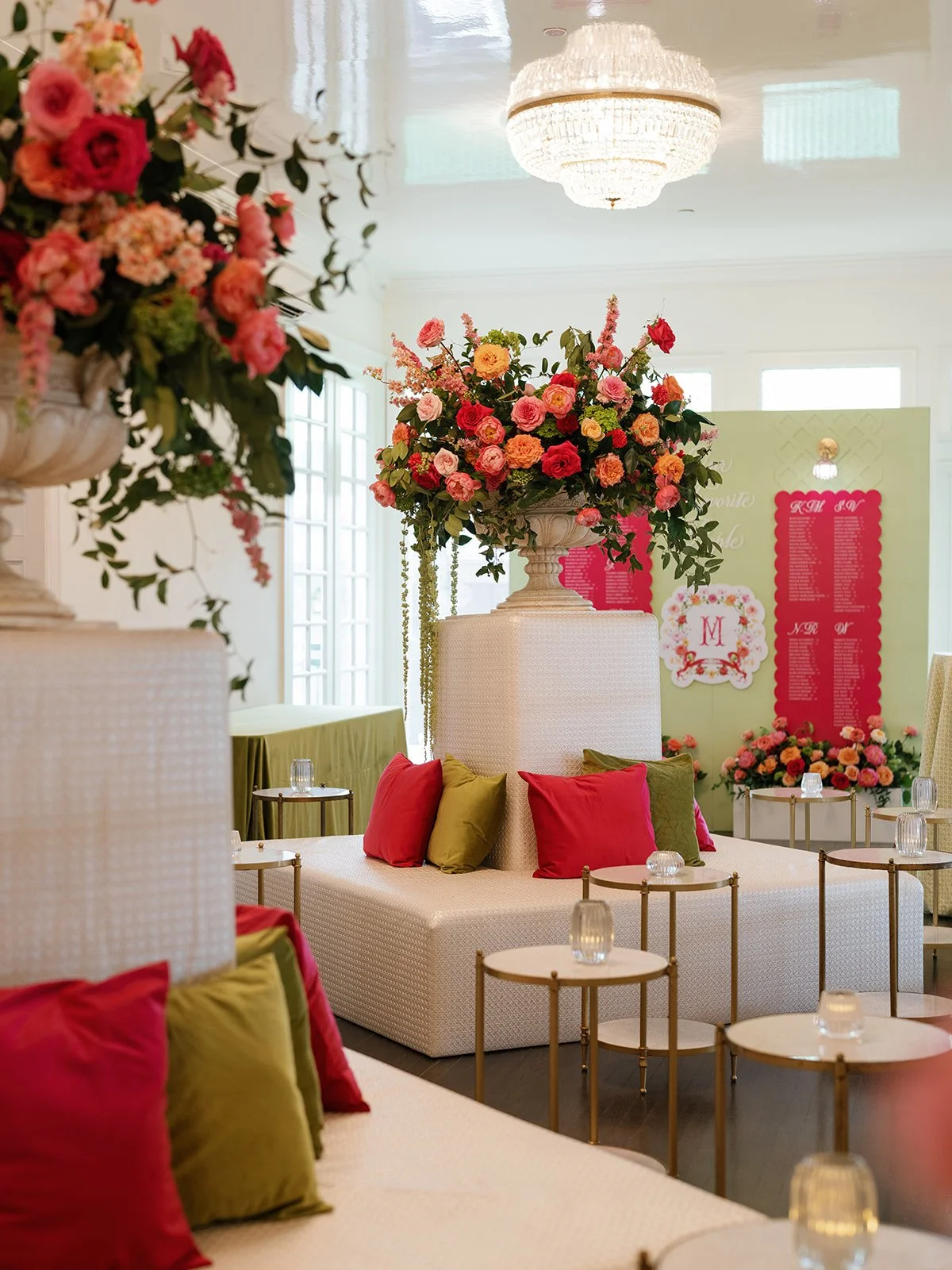  Tall pedestal floral arrangement in coral, pink, and orange beside a white tufted lounge with olive and hot pink velvet pillows at Woodbine Mansion 