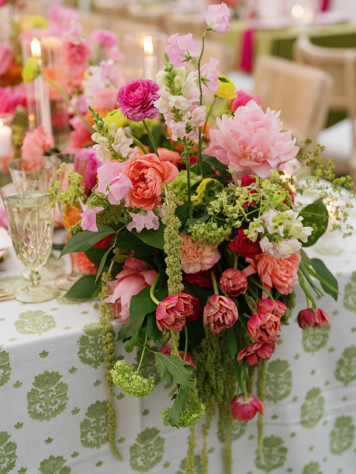  Close-up centerpiece of pink peonies, coral ranunculus, and sweet peas beside lit candles at a Woodbine Mansion reception table 